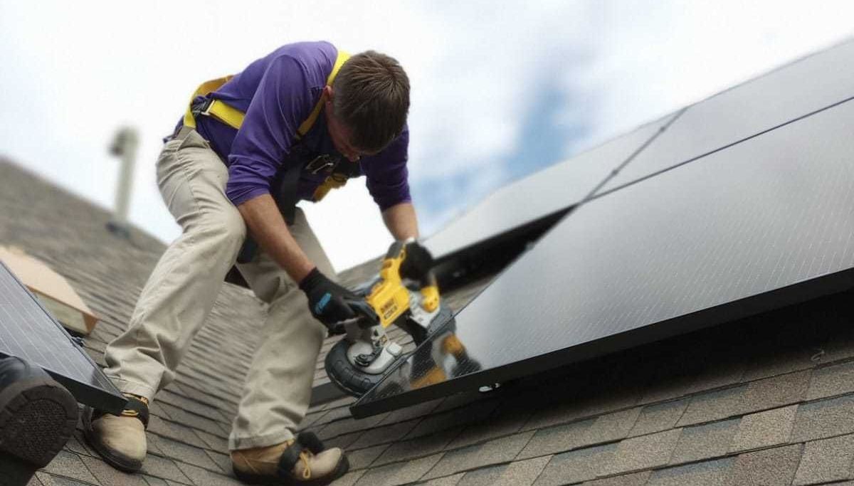 A man is installing solar panels on the roof of a house.