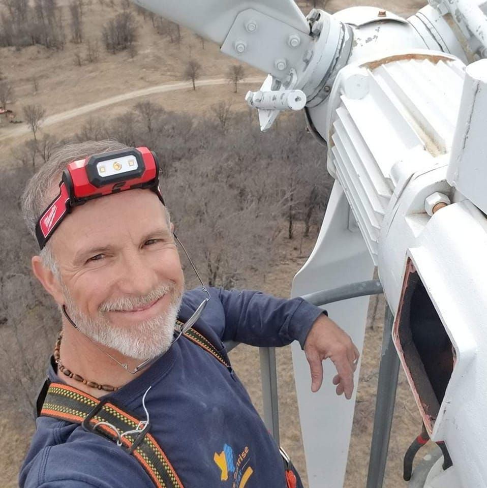 A man wearing a headlamp is standing in front of a wind turbine