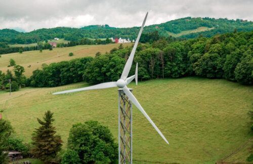 An aerial view of a wind turbine in a grassy field surrounded by trees.