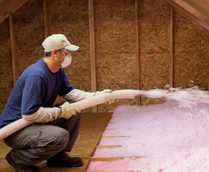 A man wearing a mask is blowing insulation into an attic.