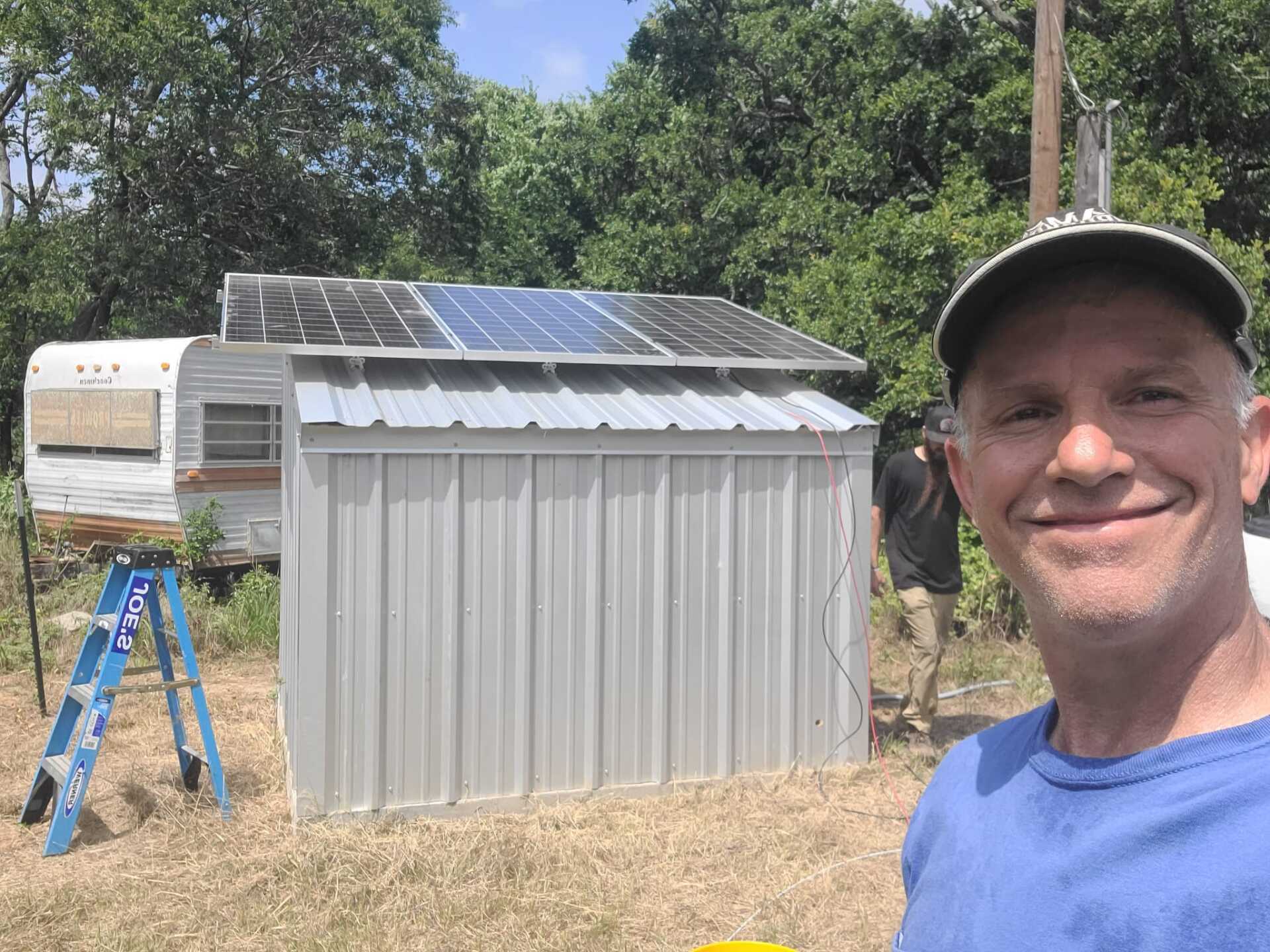 A man is standing in front of a shed with solar panels on it.
