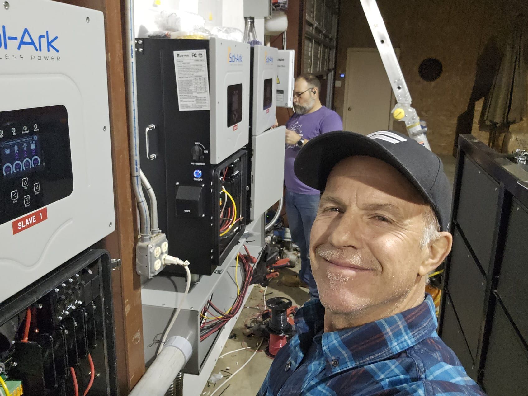A man in a plaid shirt is standing in front of a solar panel.