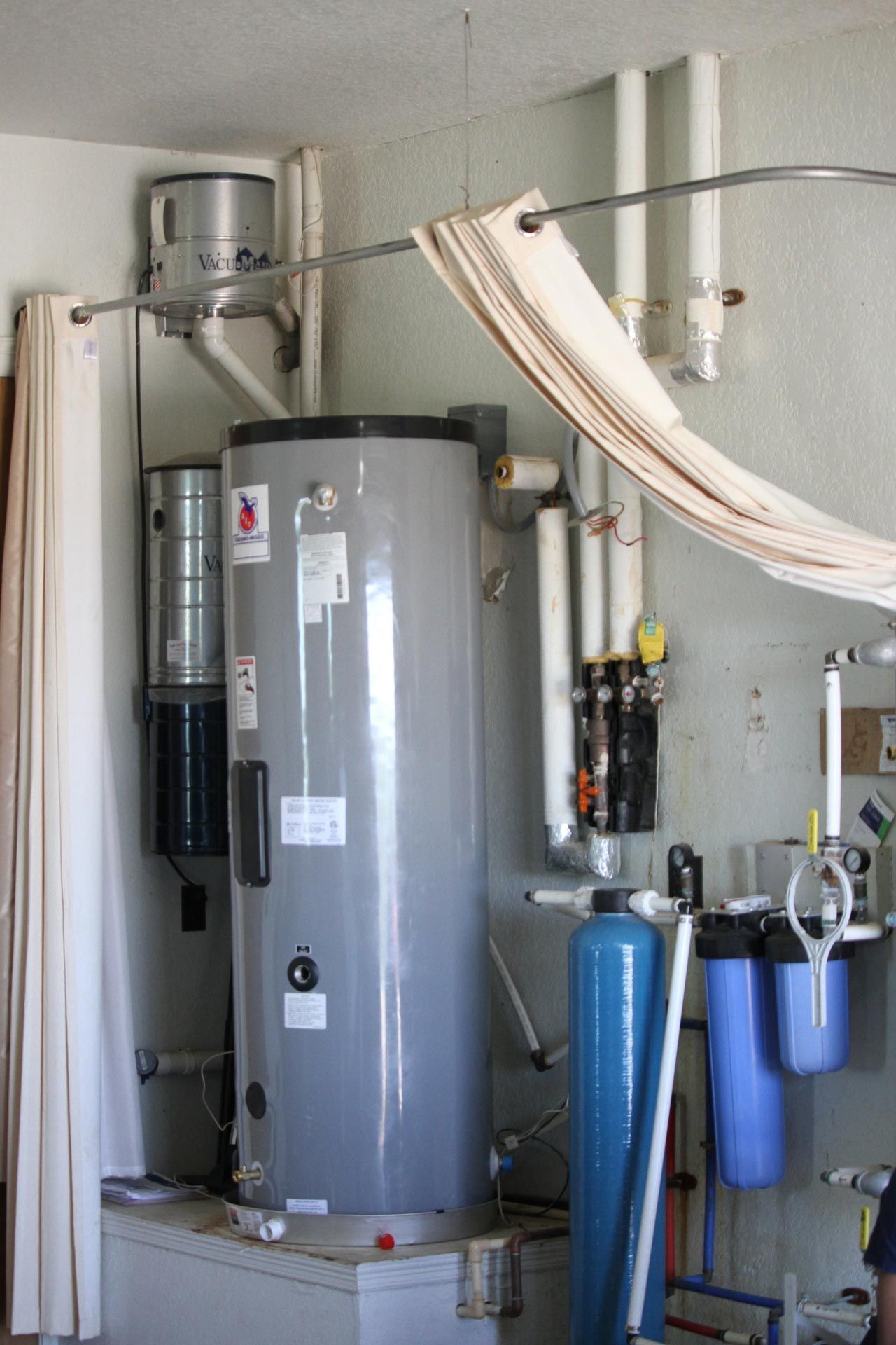 A gray water heater is in a room with pipes