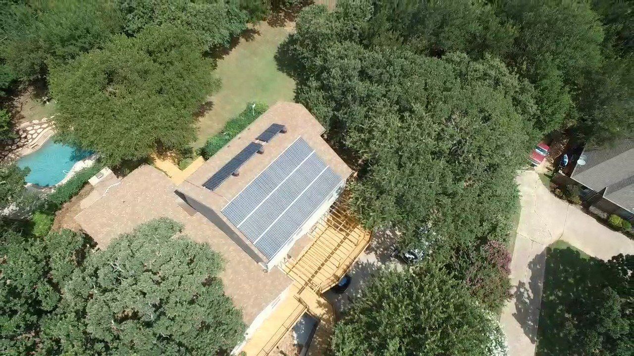 An aerial view of a house with solar panels on the roof surrounded by trees.