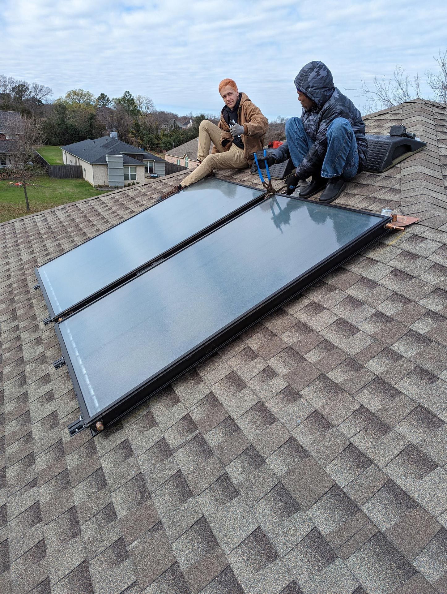 Two men are sitting on top of a roof installing solar panels.