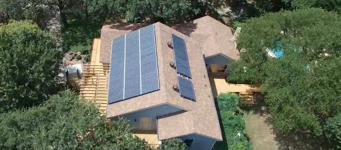 An aerial view of a house with solar panels on the roof surrounded by trees.