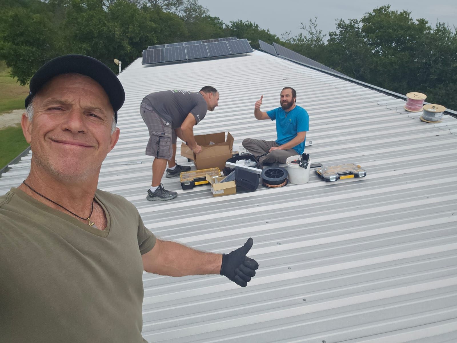 A man is giving a thumbs up while two men work on a roof.
