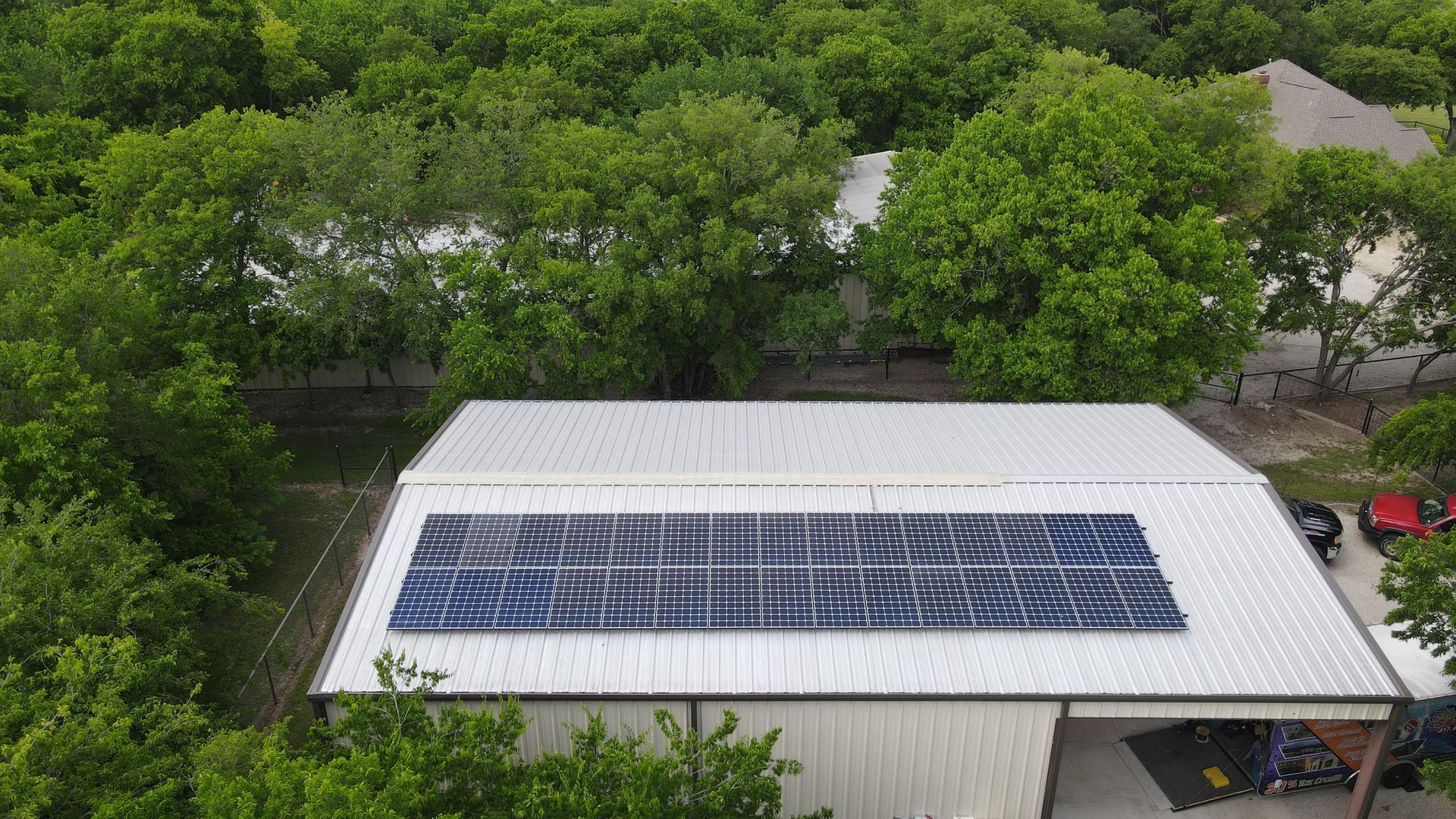An aerial view of a garage with solar panels on the roof surrounded by trees.