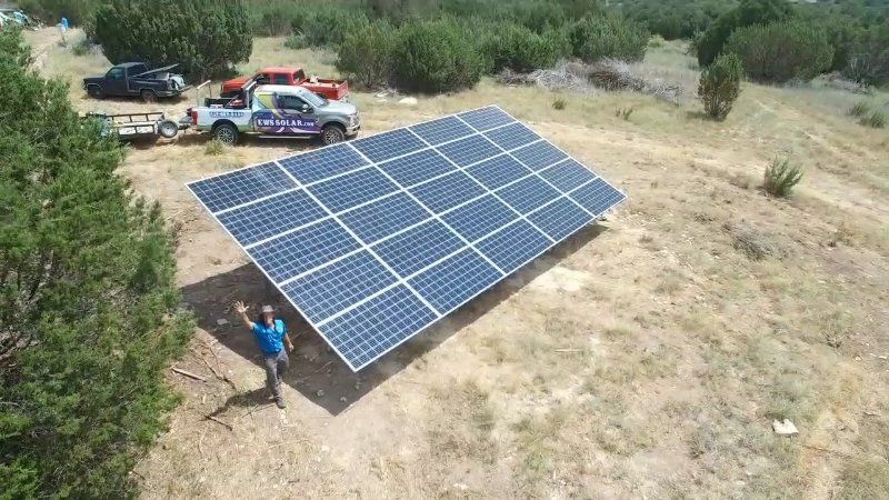 A man is standing next to a large solar panel in a field.