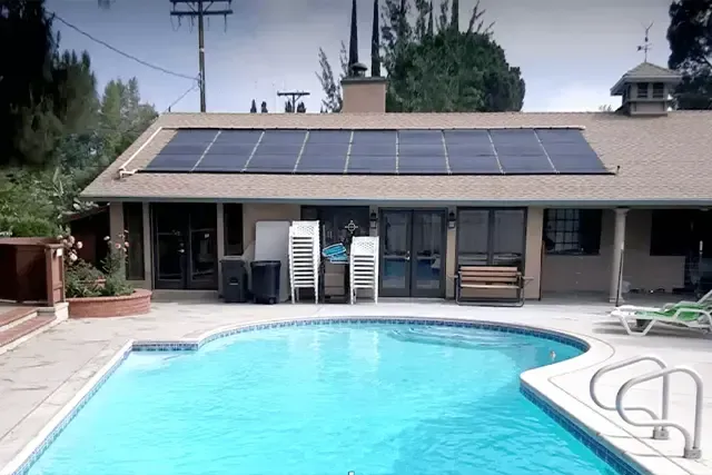 A swimming pool in front of a house with solar panels on the roof