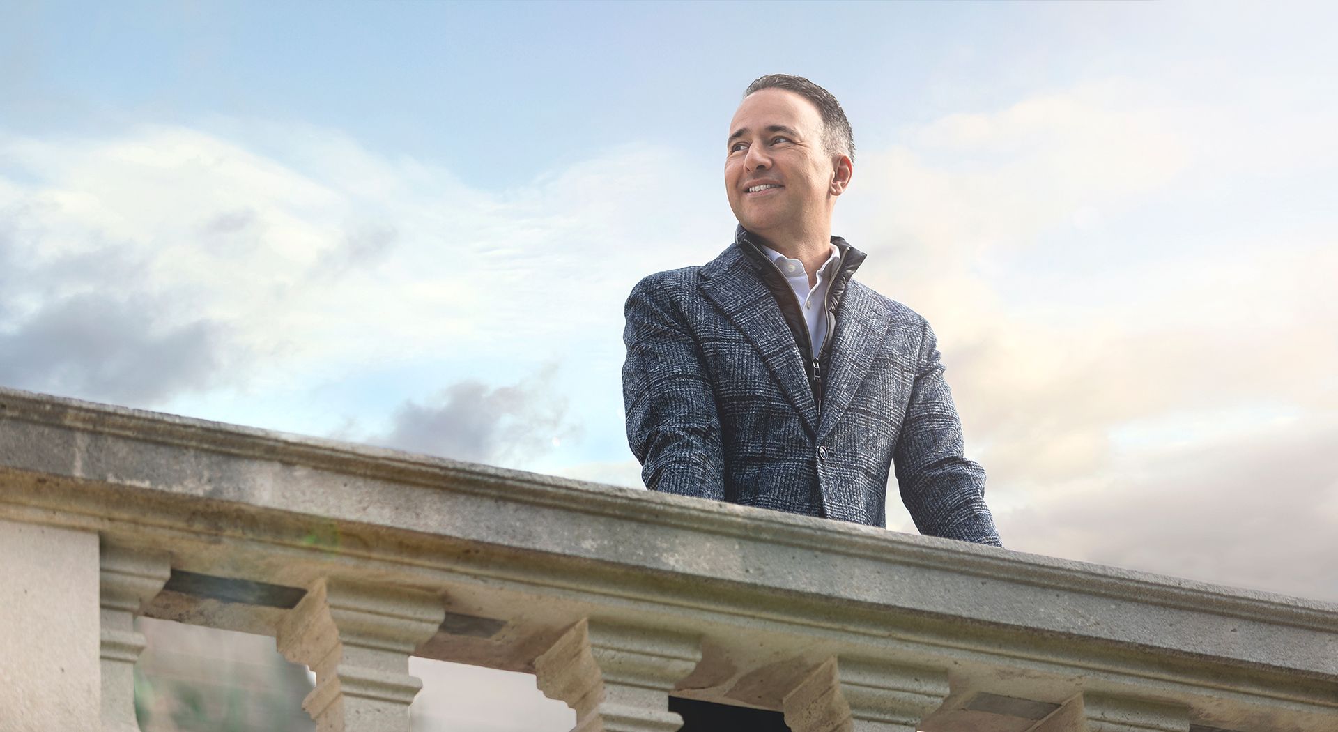 A man is standing on a balcony looking at the sky.