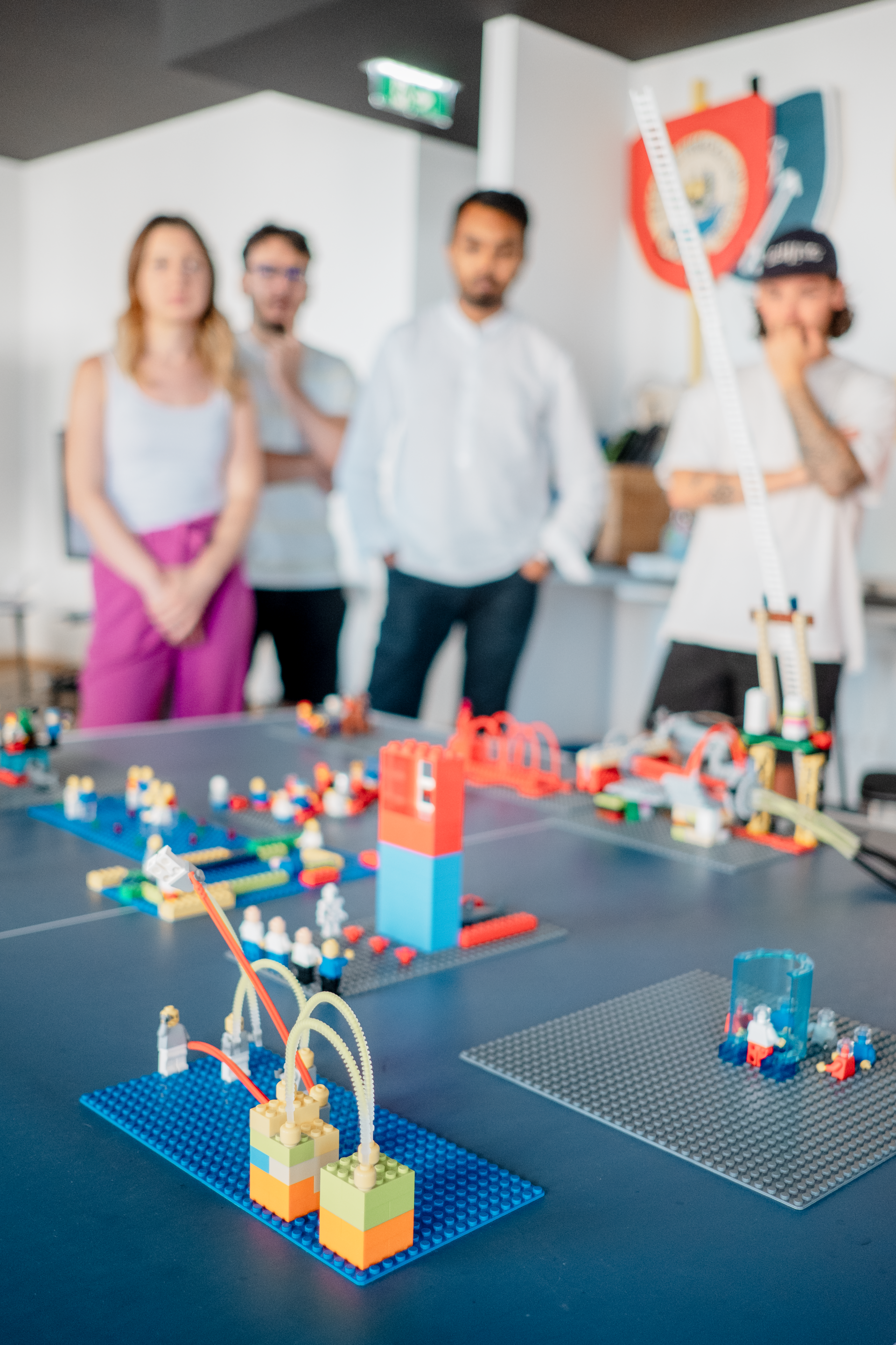 A group of people are standing around a table with lego models on it.