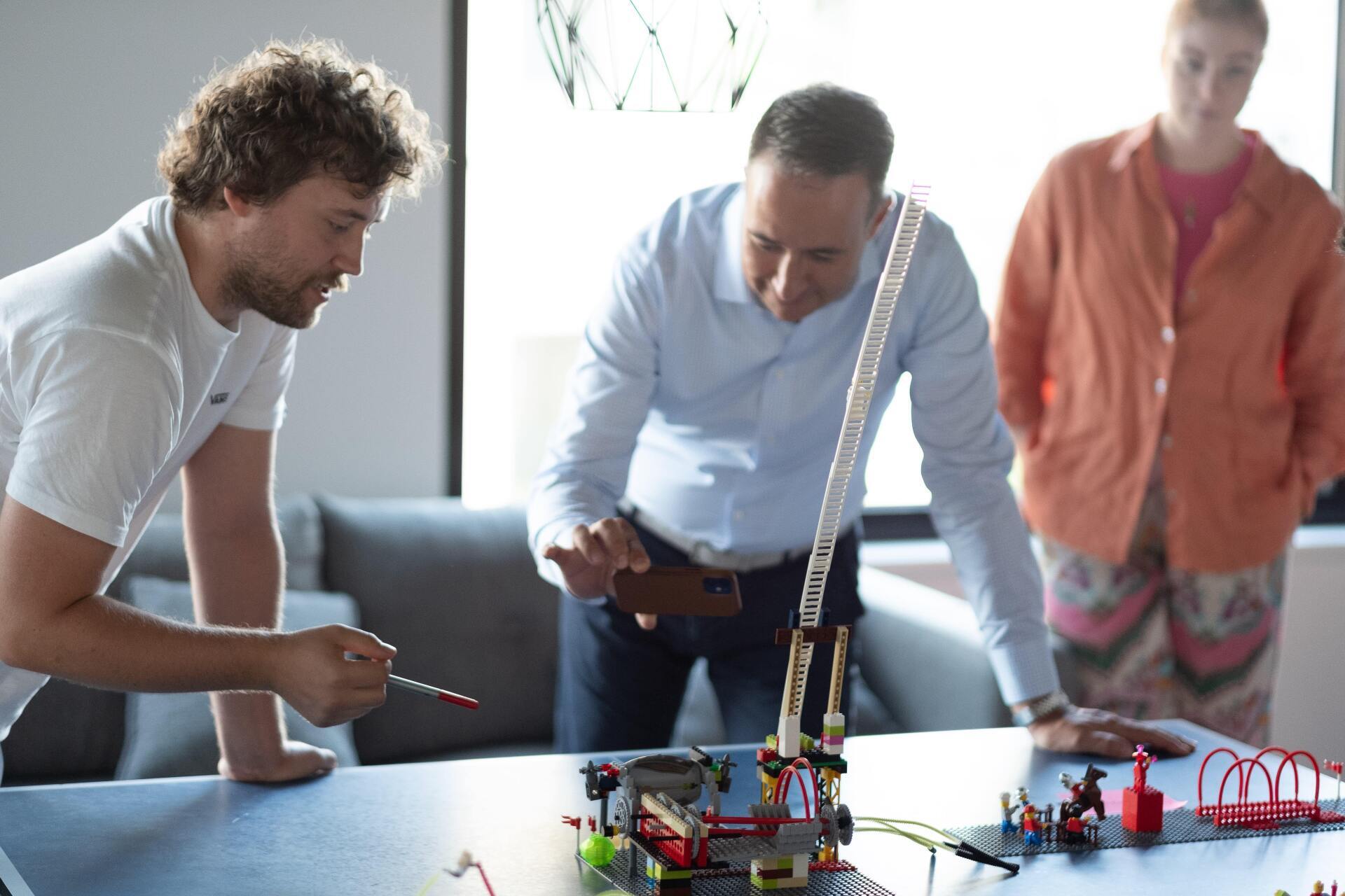 Three men are looking at a lego set on a table.
