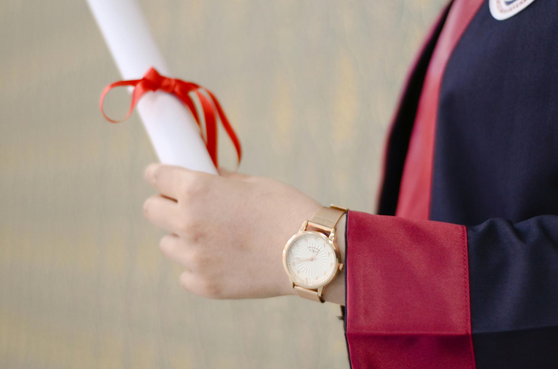 A graduate is wearing a watch and holding a diploma.