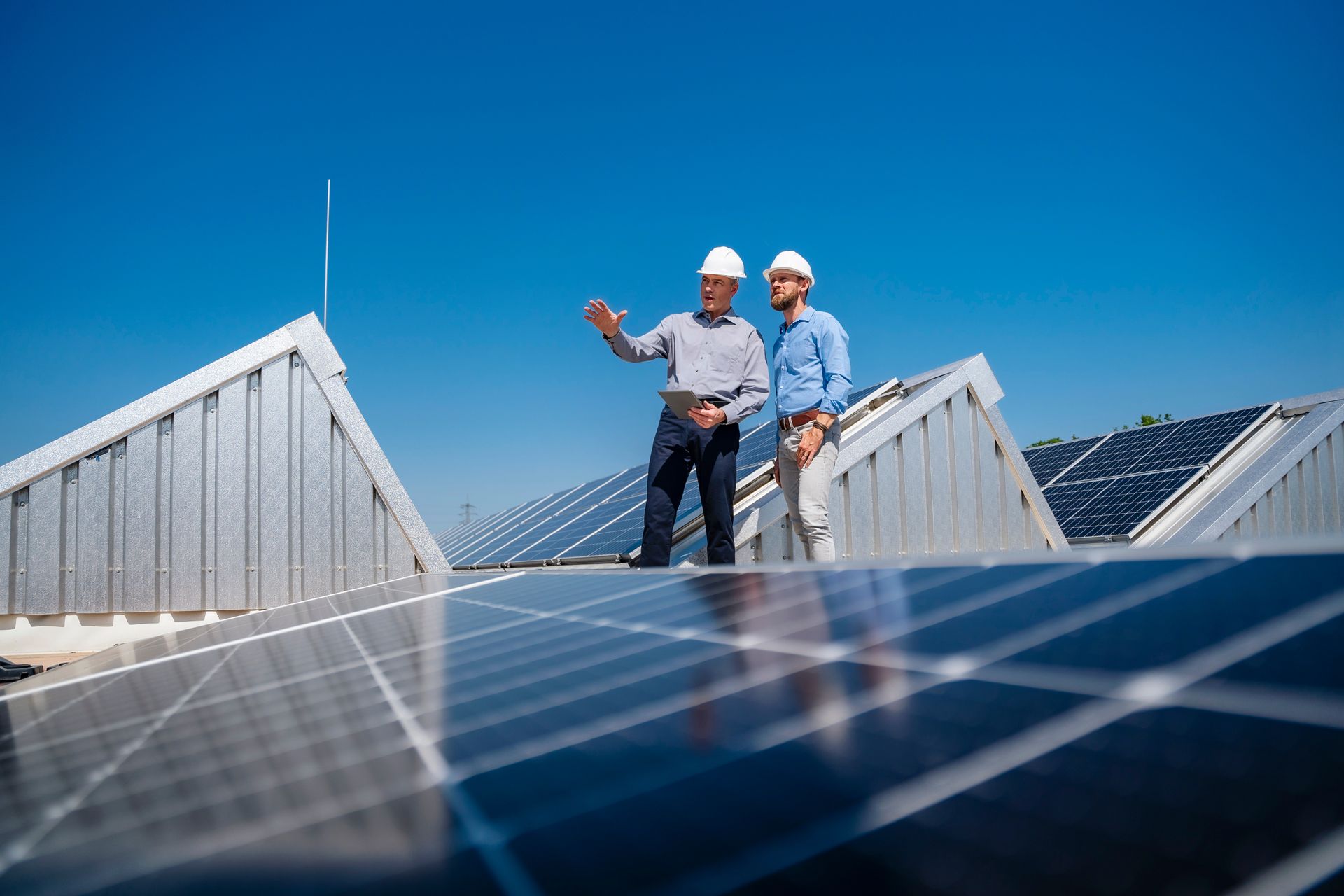 Two engineers wearing hard hats having a meeting on the roof of a building with solar panels. Two engineers wearing hard hats having a meeting on the roof of a building with solar panels.
