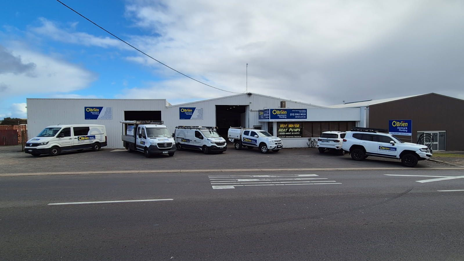 Vehicles parked outside a white commercial building under a partly cloudy sky.