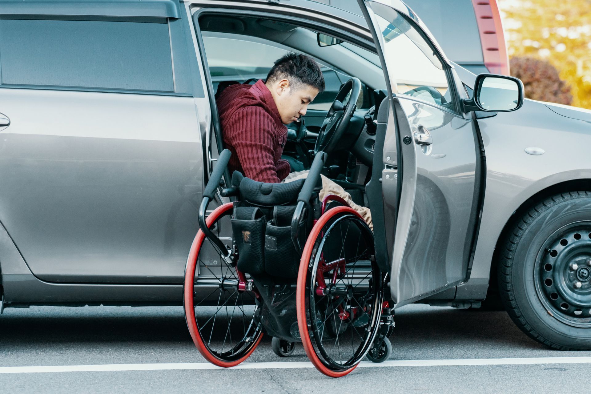 Man in a wheelchair transferring from a silver van with the side door open