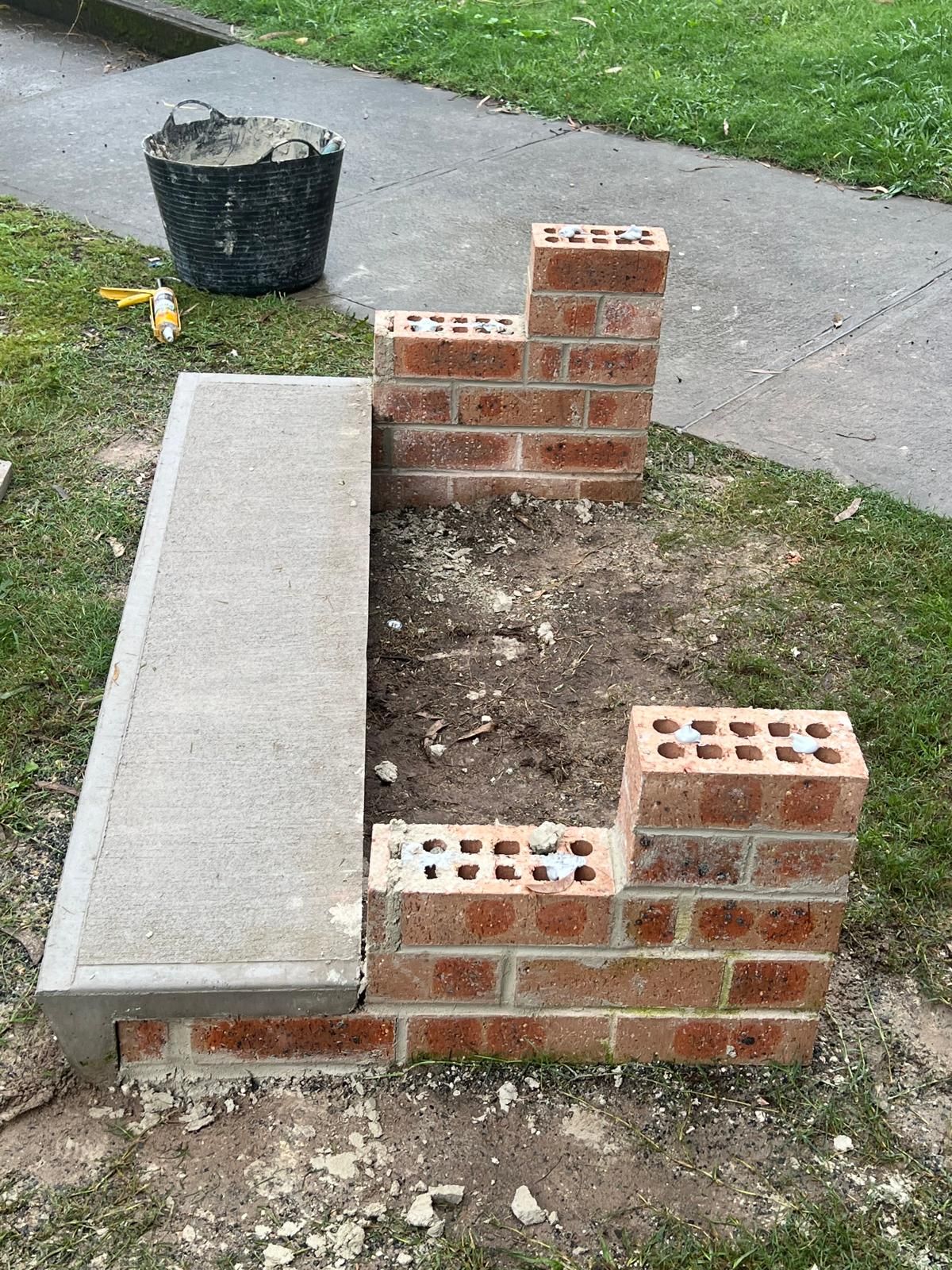 A brick wall is being built next to a concrete bench.