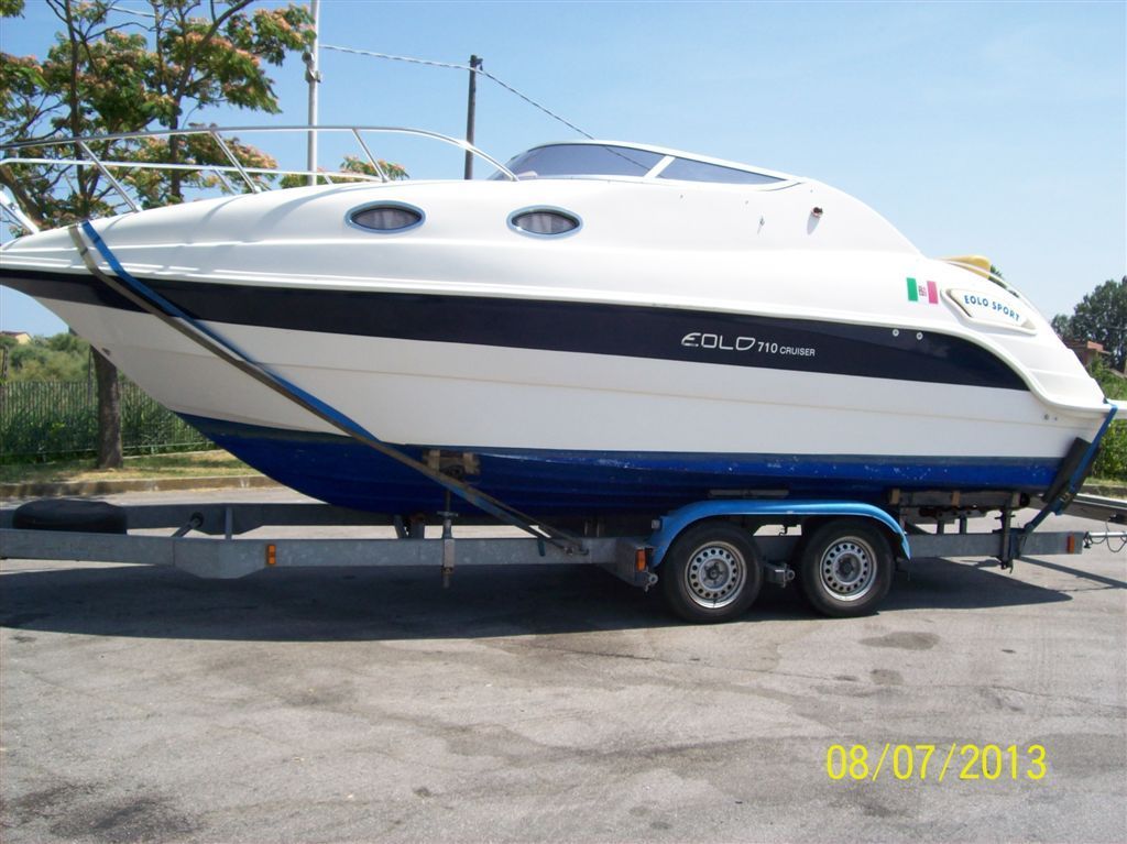 Motoscafo bianco con scafo blu su rimorchio. Adesivo con bandiera italiana visibile.