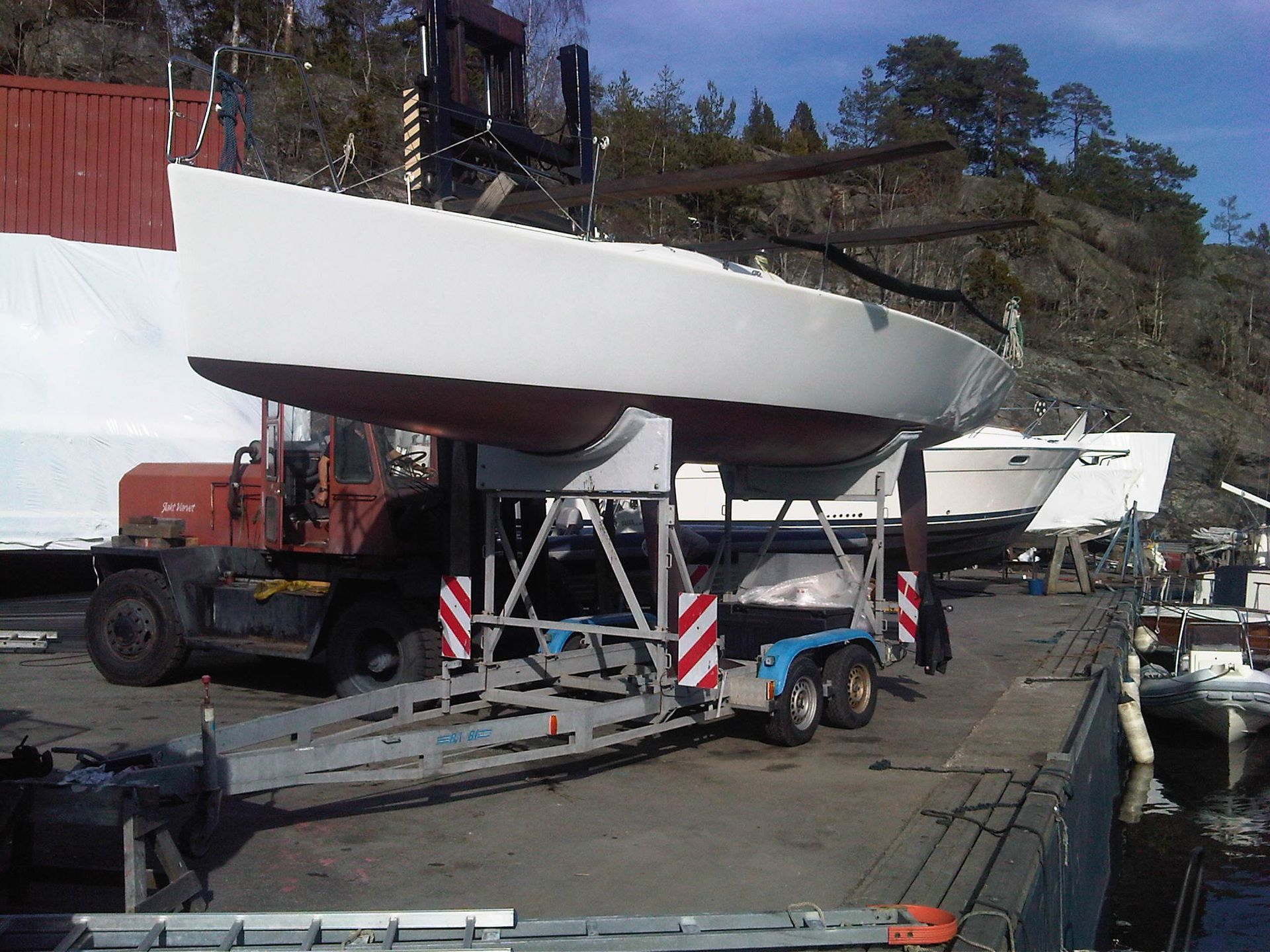 Una barca a vela bianca viene caricata su un rimorchio con un carrello elevatore presso un molo.