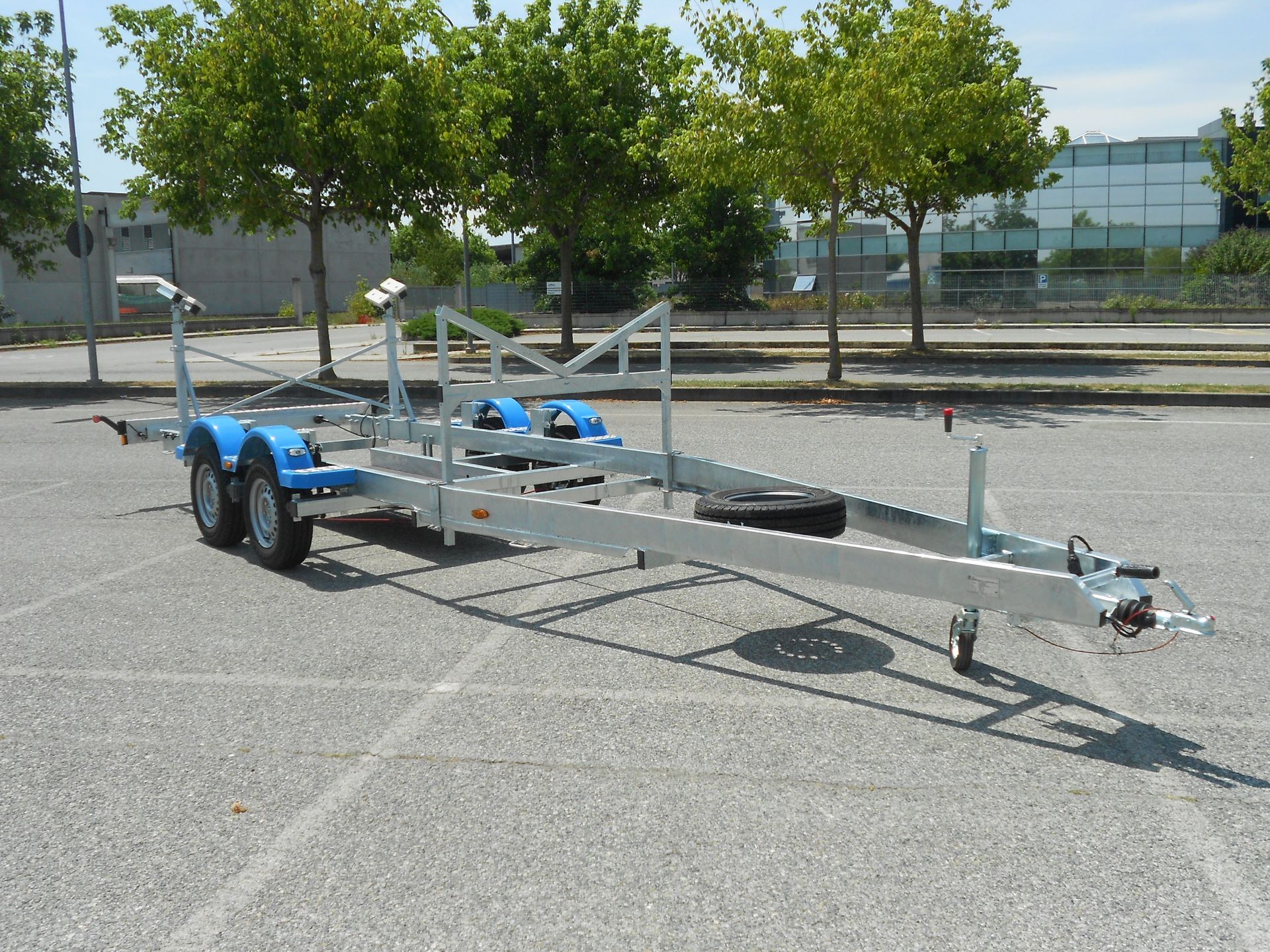 Rimorchio per barca su asfalto, parabordi blu, ruota di scorta, parcheggiato in un parcheggio all'aperto.