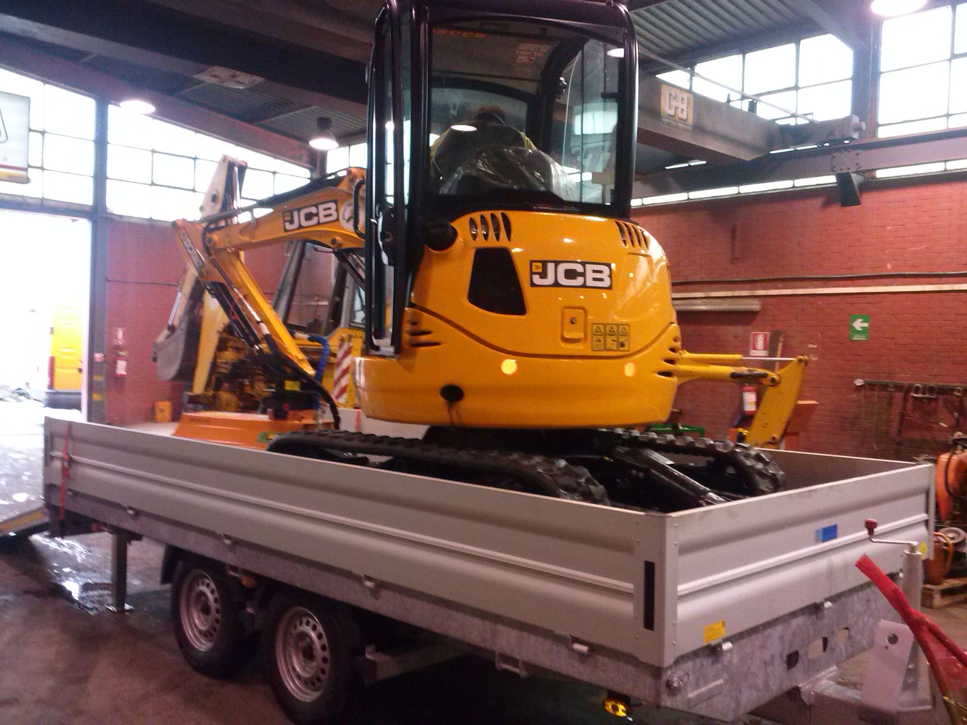 Escavatore JCB giallo su un rimorchio argentato all'interno di un garage.
