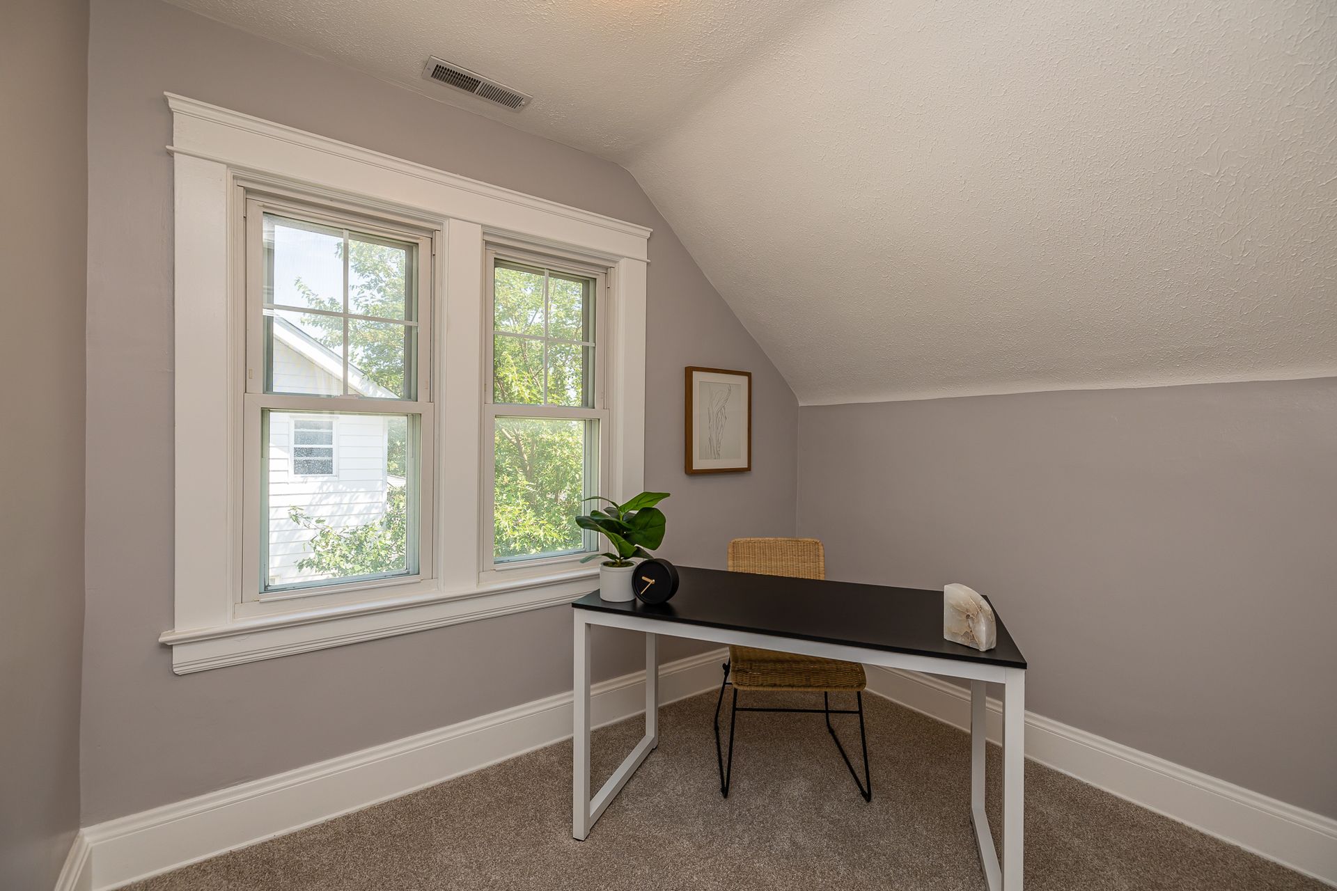 A small office space in a room with a sloped ceiling, desk, chair, and window.