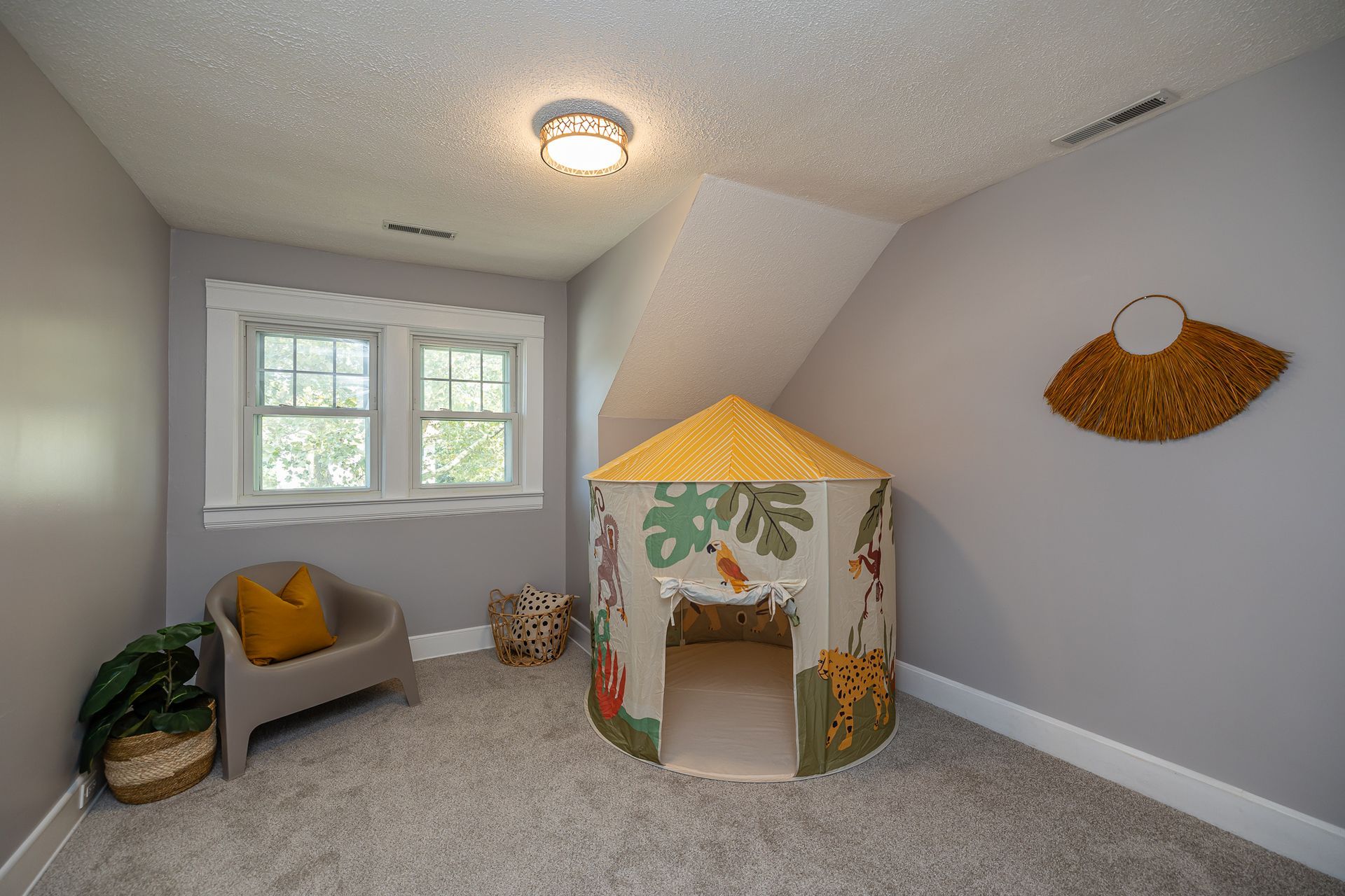 Child's bedroom with gray walls, play tent, chair, window, and decorative wall hanging.