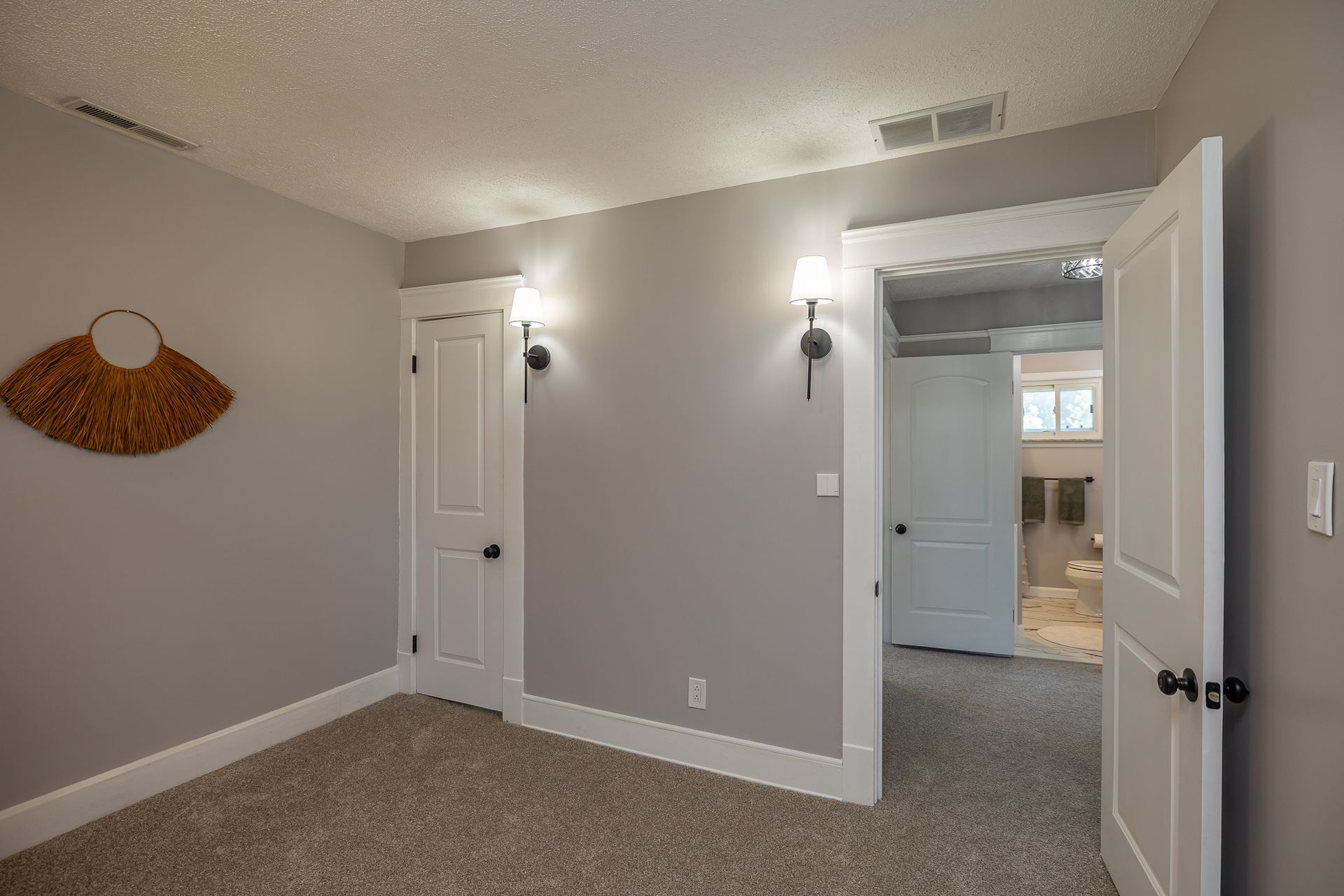 Bedroom with gray walls, white trim, two doors, wall sconces, and woven wall decor.