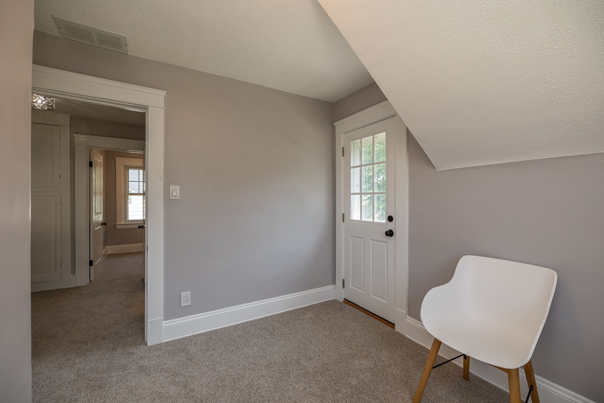 Empty room with gray walls, white trim, door, and chair.