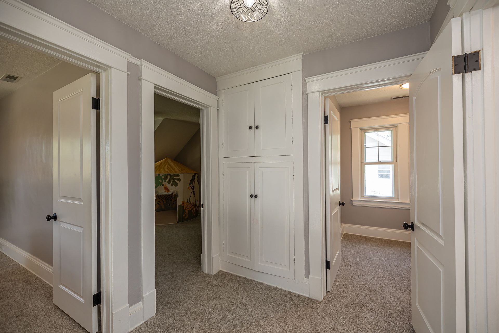 Hallway with three doorways, closet, and carpeted floor; white trim and gray walls.