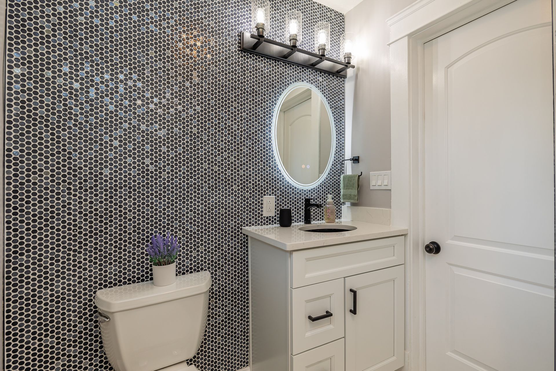 Modern bathroom with black and white patterned tile, white vanity, and round mirror.