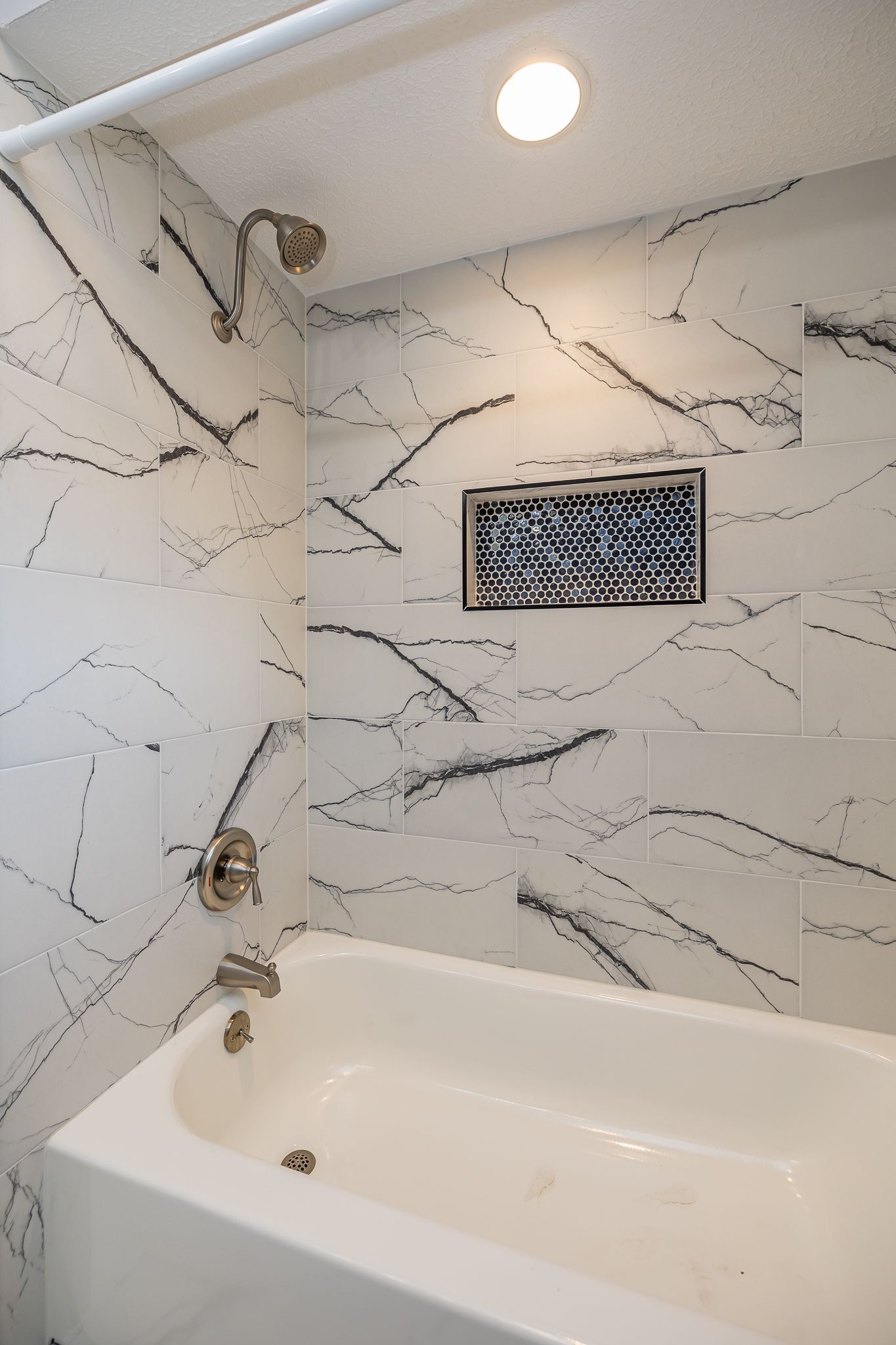 White bathtub with marble-like tile walls and a silver showerhead and faucet.
