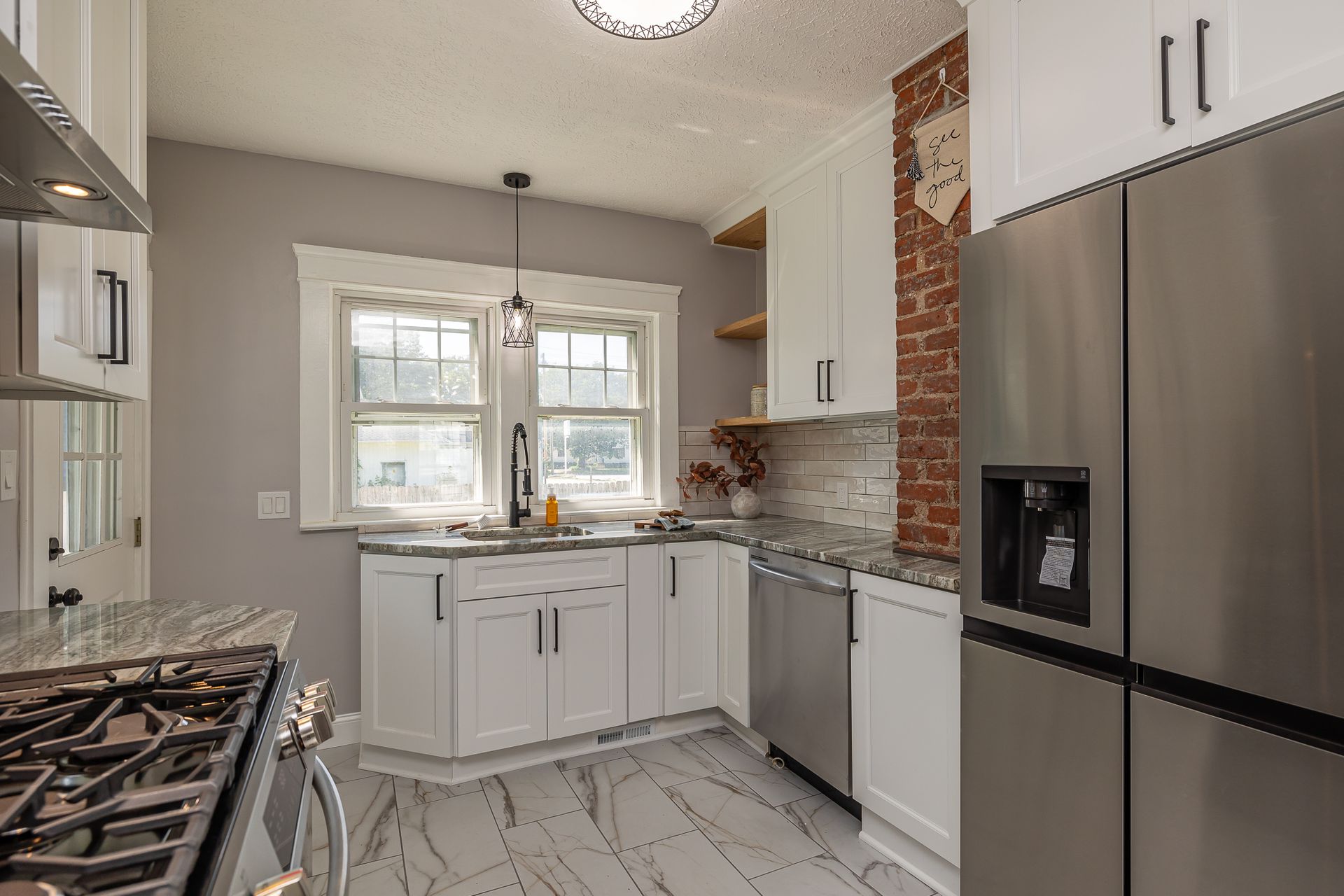 Kitchen with white cabinets, stainless steel appliances, exposed brick, and a window.
