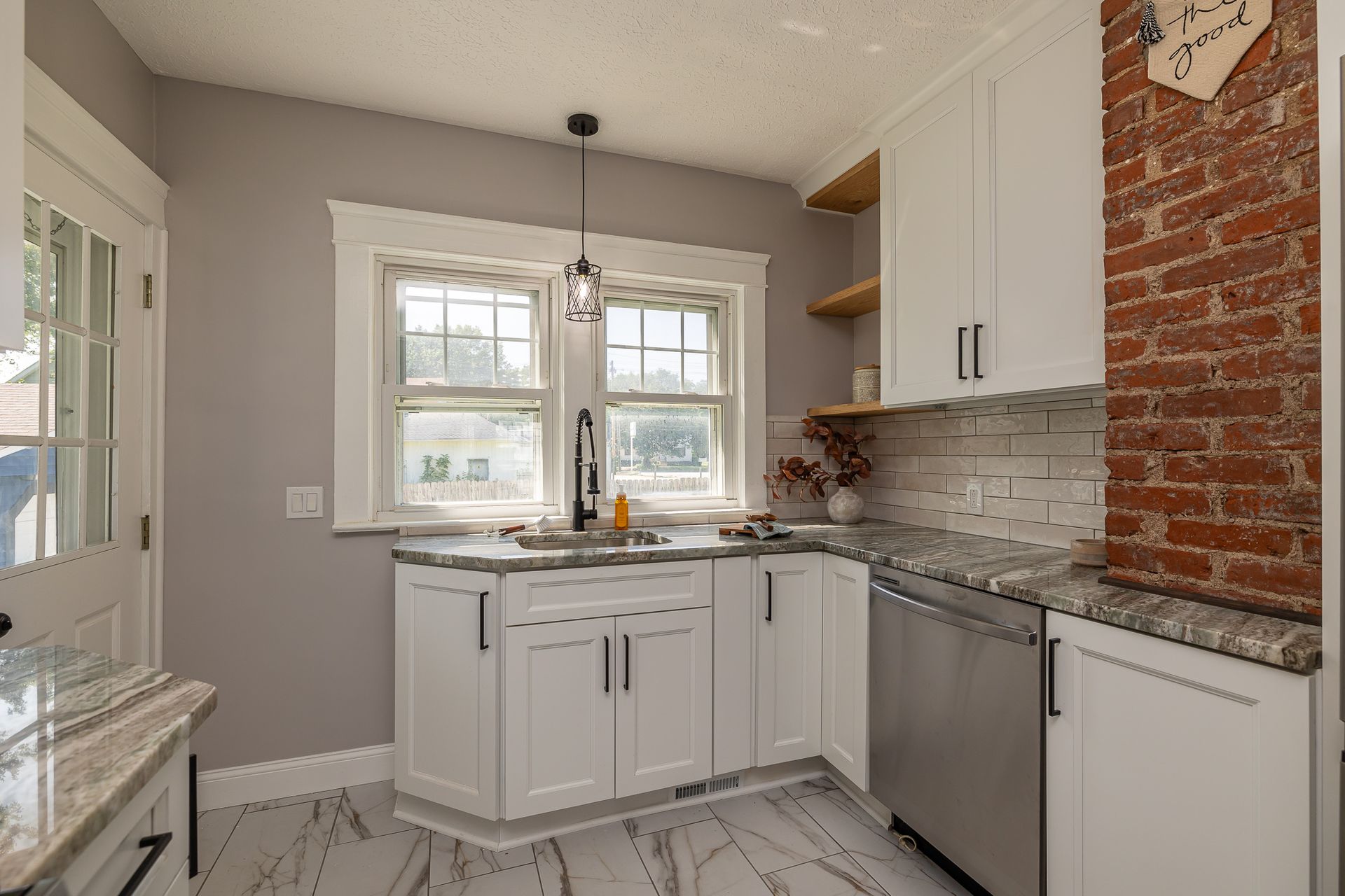 Kitchen with white cabinets, stainless steel appliances, exposed brick, and a window above the sink.