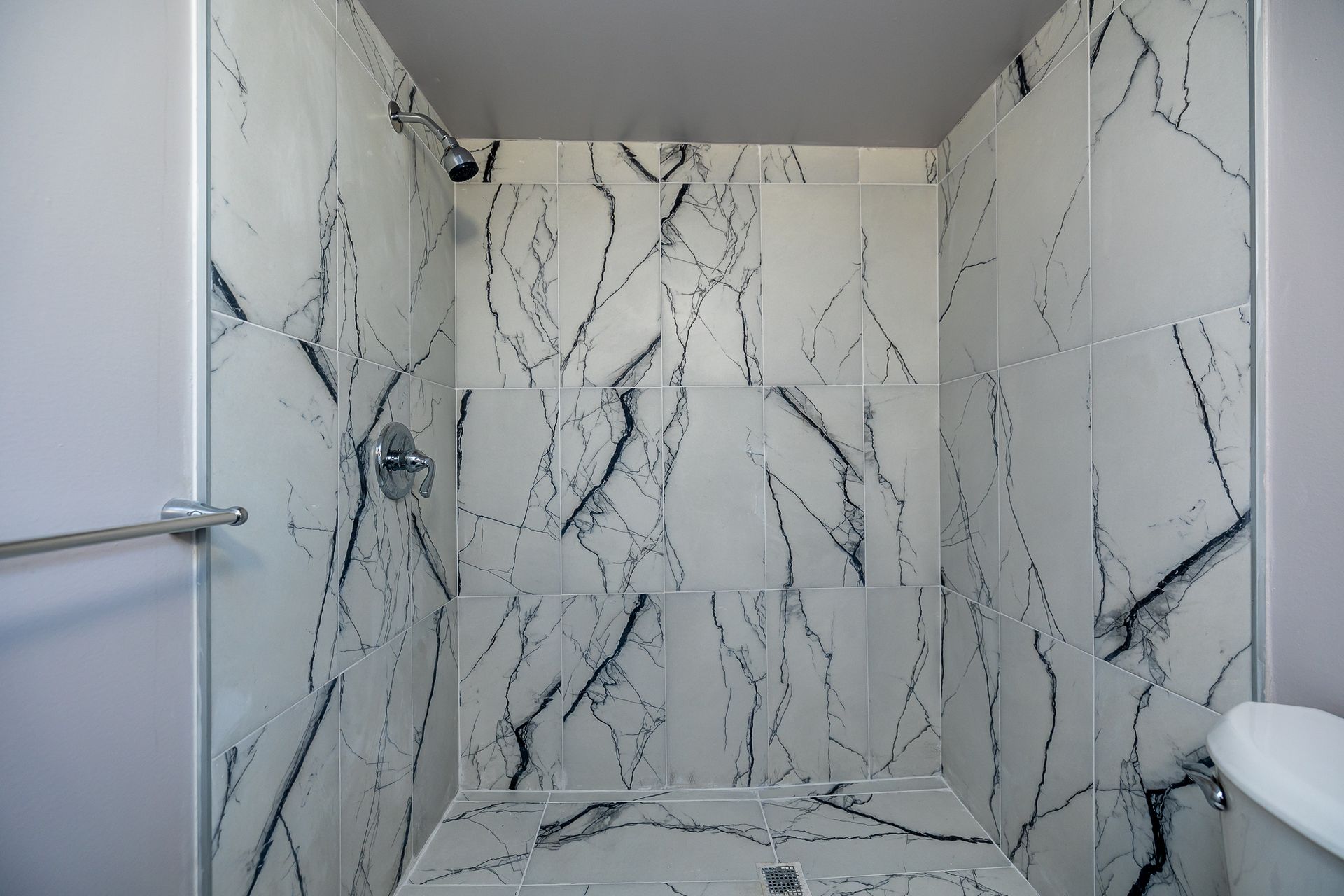 Shower with white marble-patterned tile, chrome fixtures, and a gray wall.