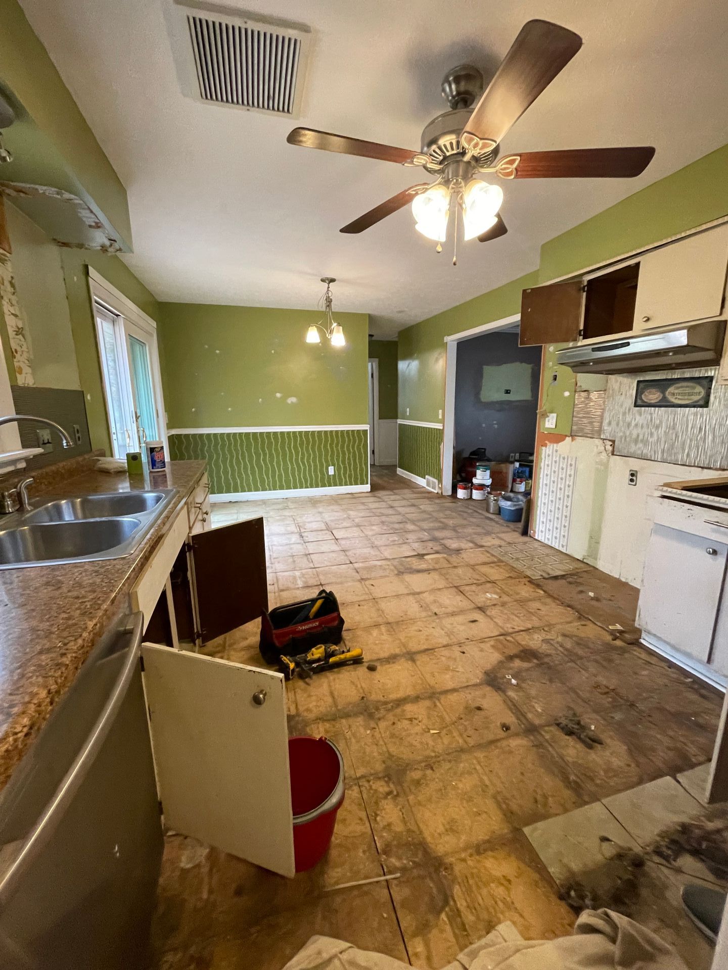 Kitchen under renovation, featuring exposed floorboards, partial cabinetry, and green walls.
