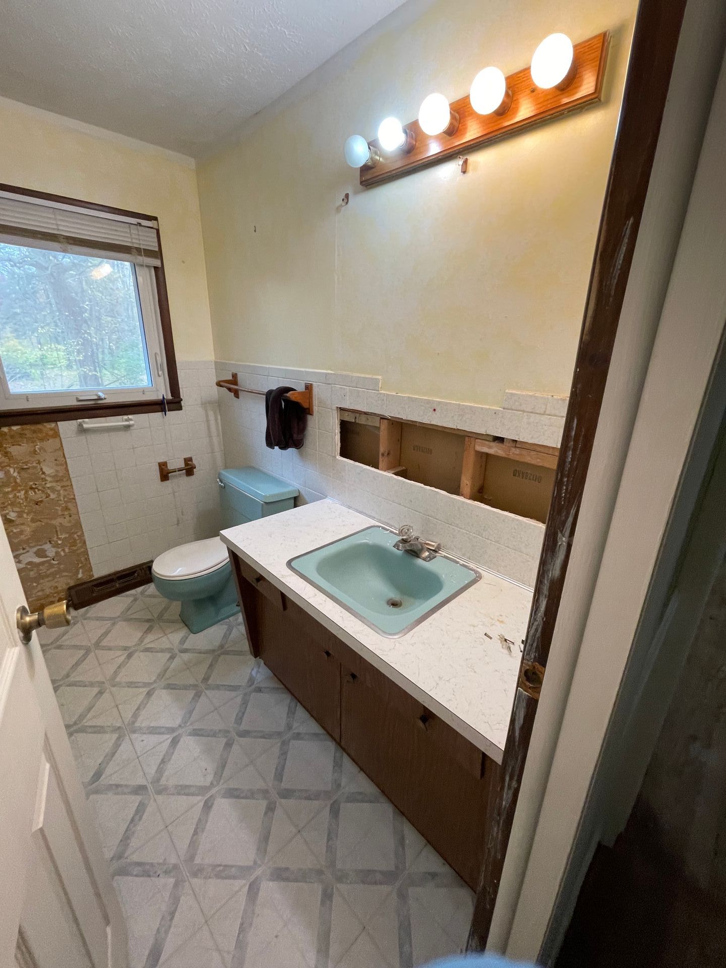 Bathroom with a teal sink, toilet, and a window. Beige and brown walls, patterned floor.