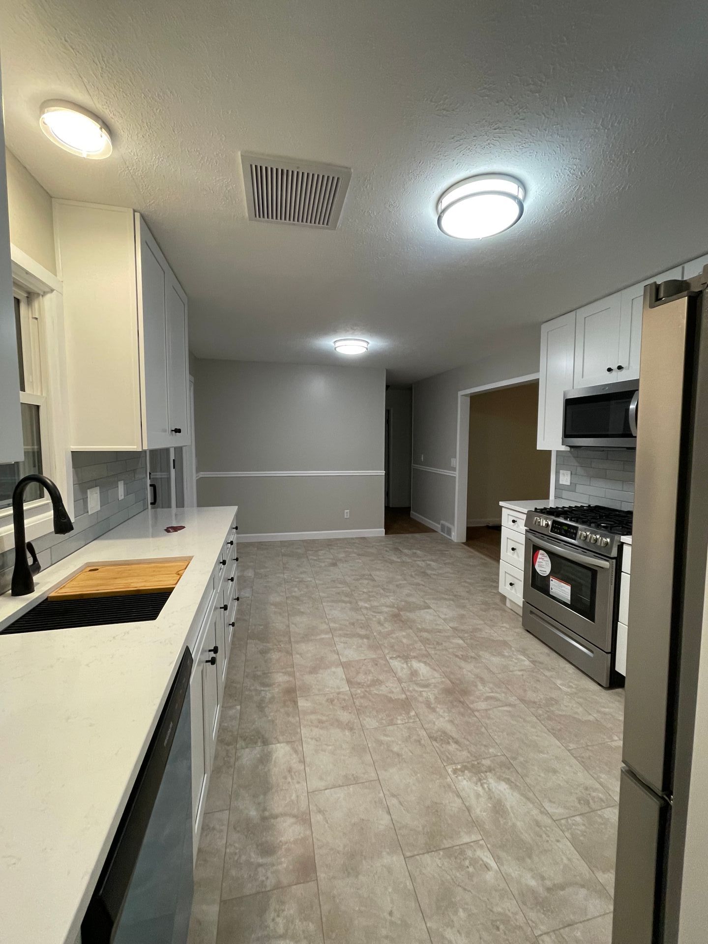 Modern kitchen renovation with white cabinets, gray walls, stainless steel appliances, and light flooring.