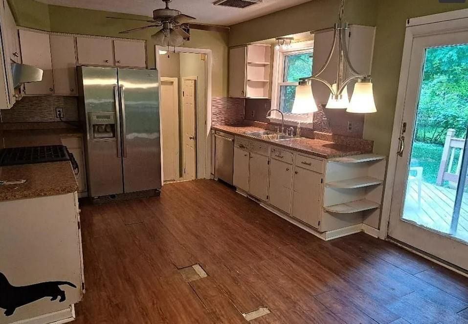 Kitchen with wooden floor, stainless steel fridge, white cabinets, and a door to a deck.