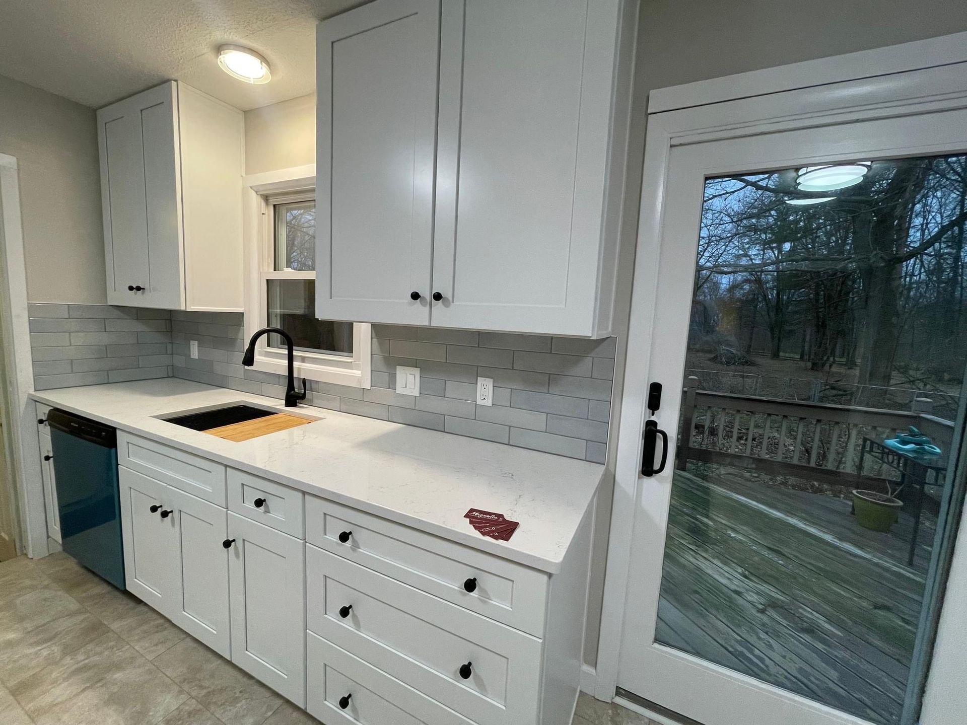 White kitchen with cabinets, countertop, black faucet, and a glass door to a deck.