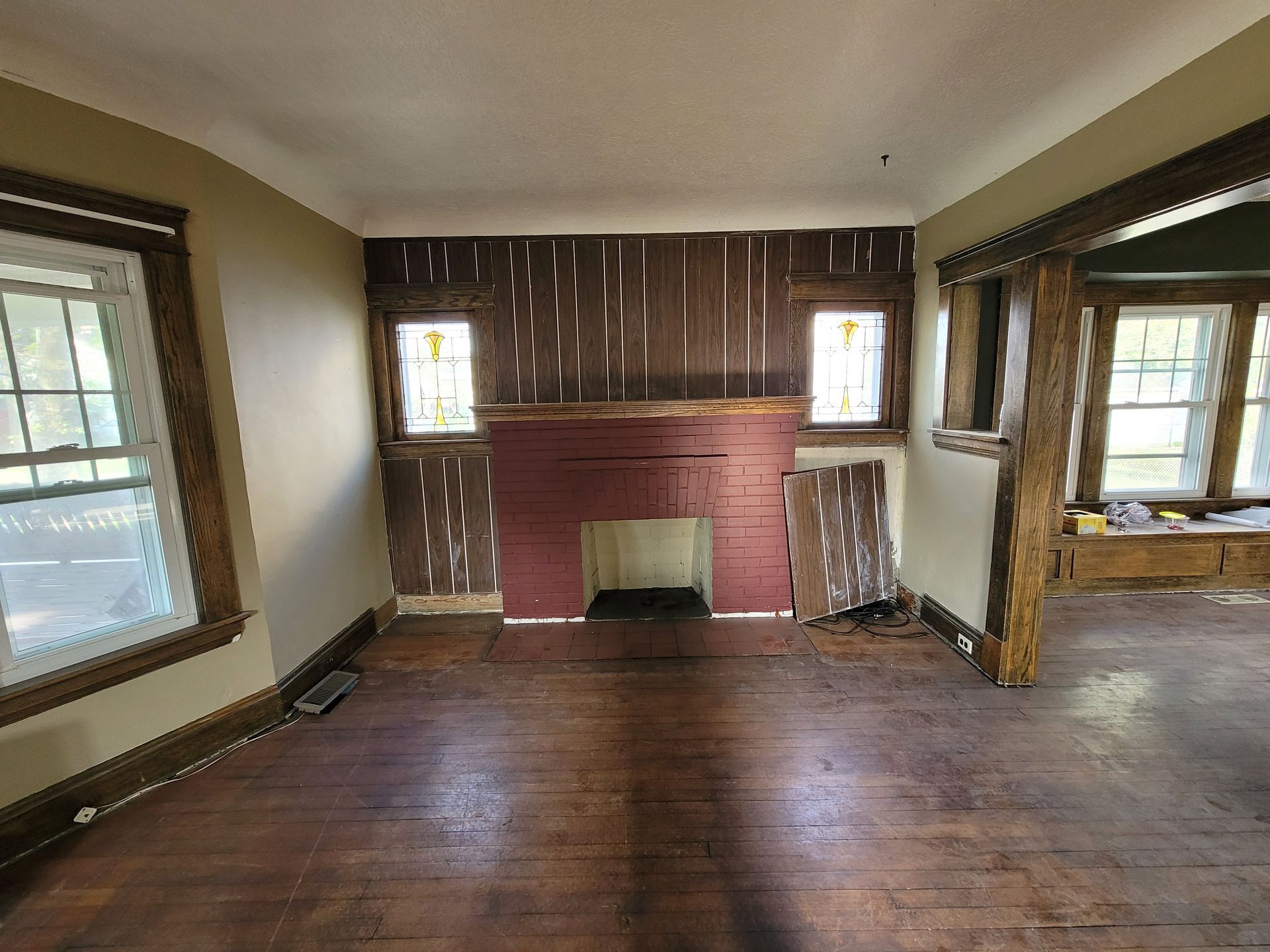 Living room with fireplace, exposed wall. Brown wood floors, red brick fireplace, stained glass windows.