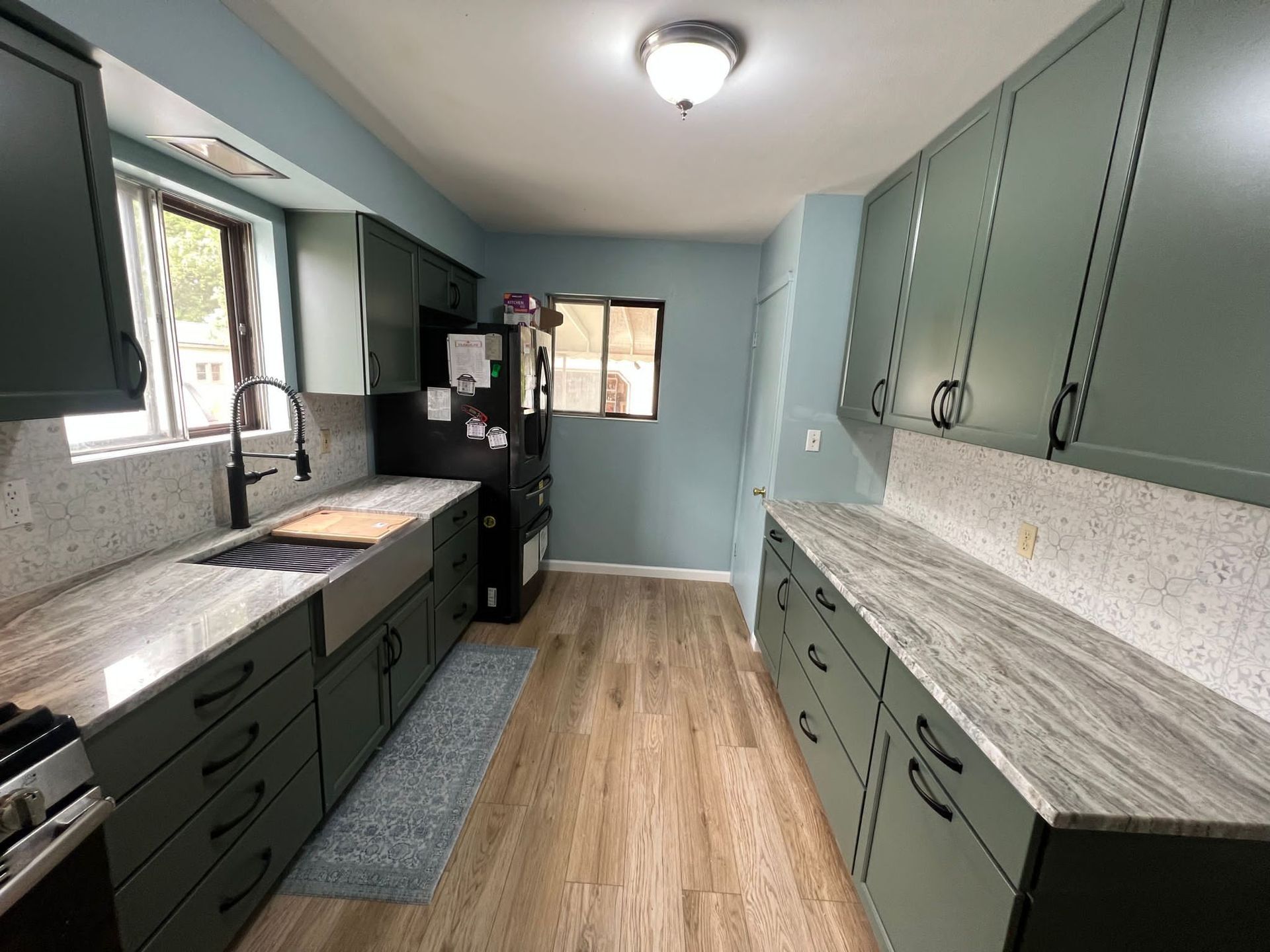 Green kitchen with light countertops and wooden floors.