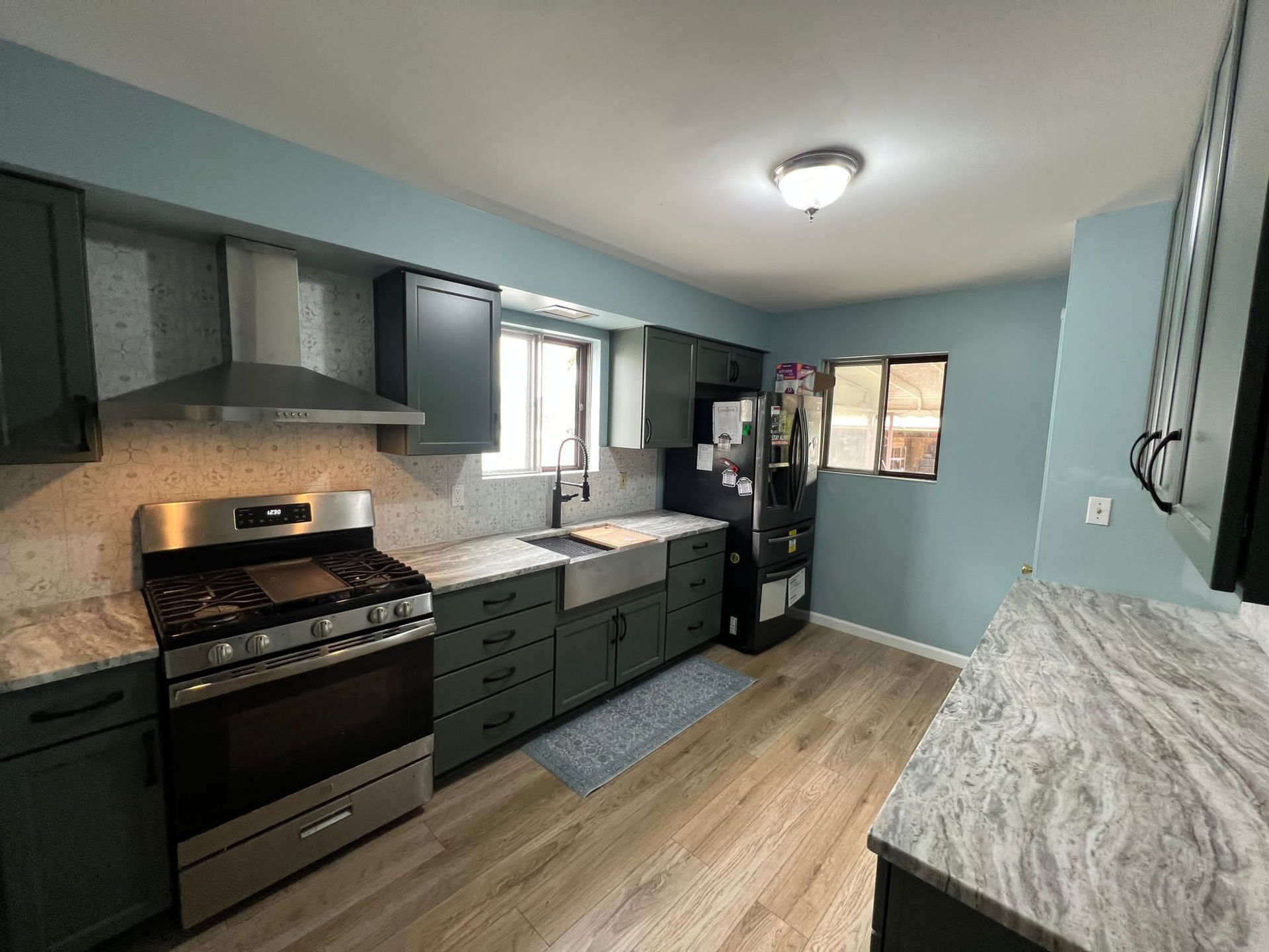 Kitchen with green cabinets, stainless steel appliances, light countertops, and blue walls.