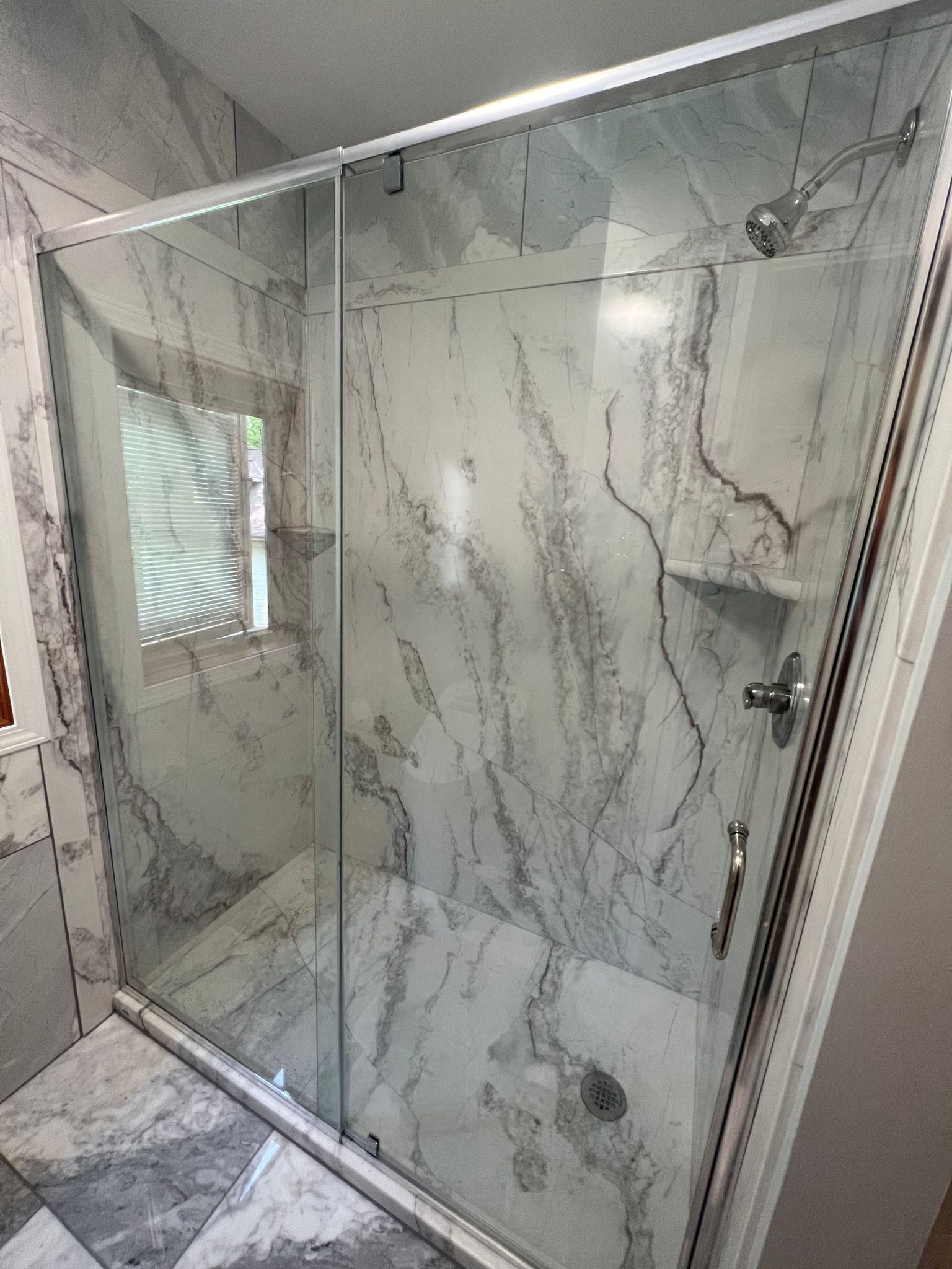 Glass shower enclosure with marble-patterned tile, chrome hardware, and a showerhead.