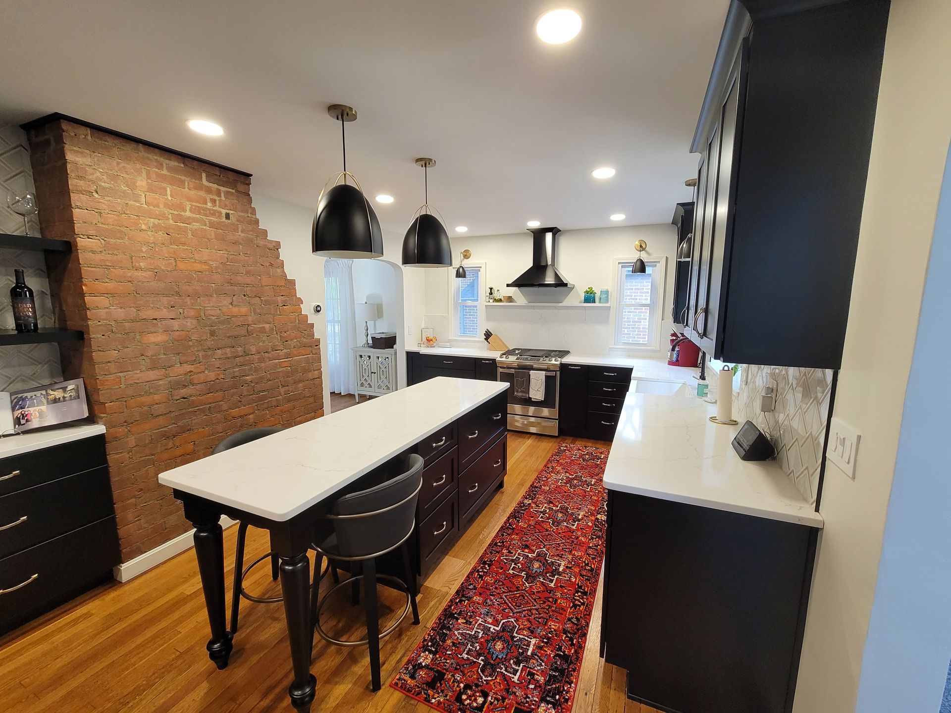 Kitchen with exposed brick wall, black cabinets, island with seating, and pendant lights.