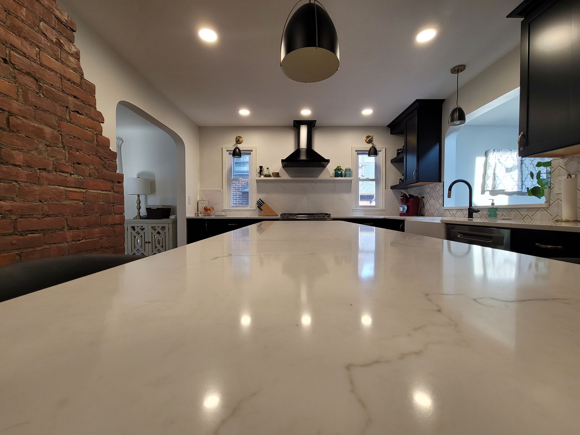 Modern kitchen with marble countertop, exposed brick, black cabinets, and a range hood.
