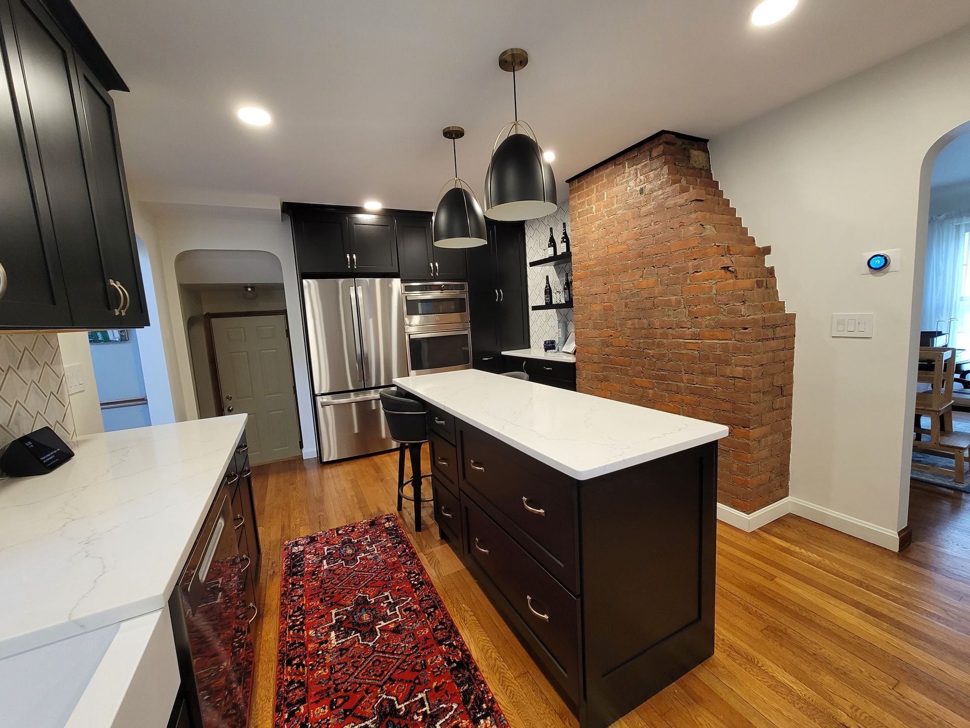 Modern kitchen with black cabinets, white countertops, island, exposed brick wall, and pendant lights.