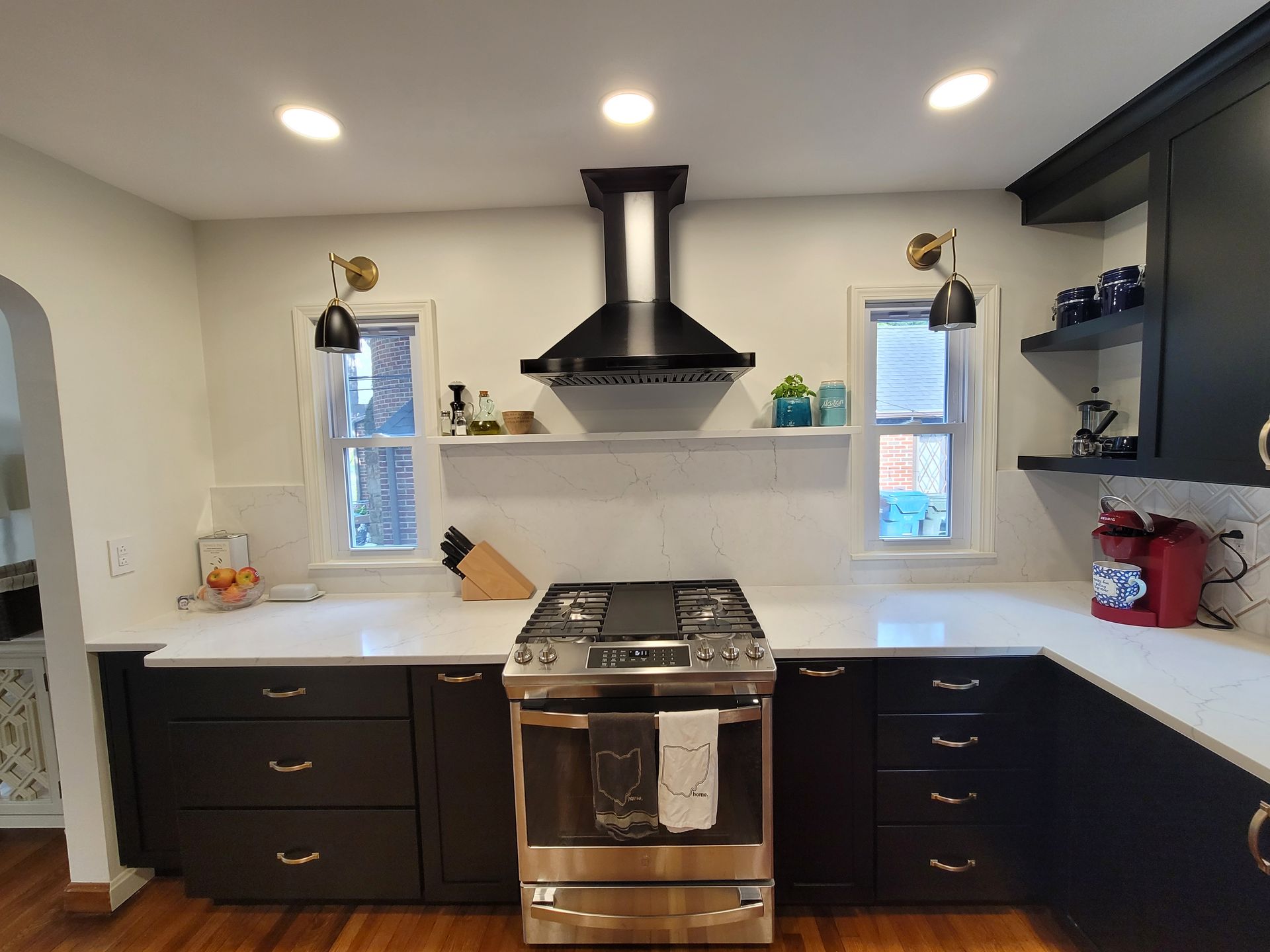 Modern kitchen with dark cabinets, white countertops, stainless steel stove, and black range hood.