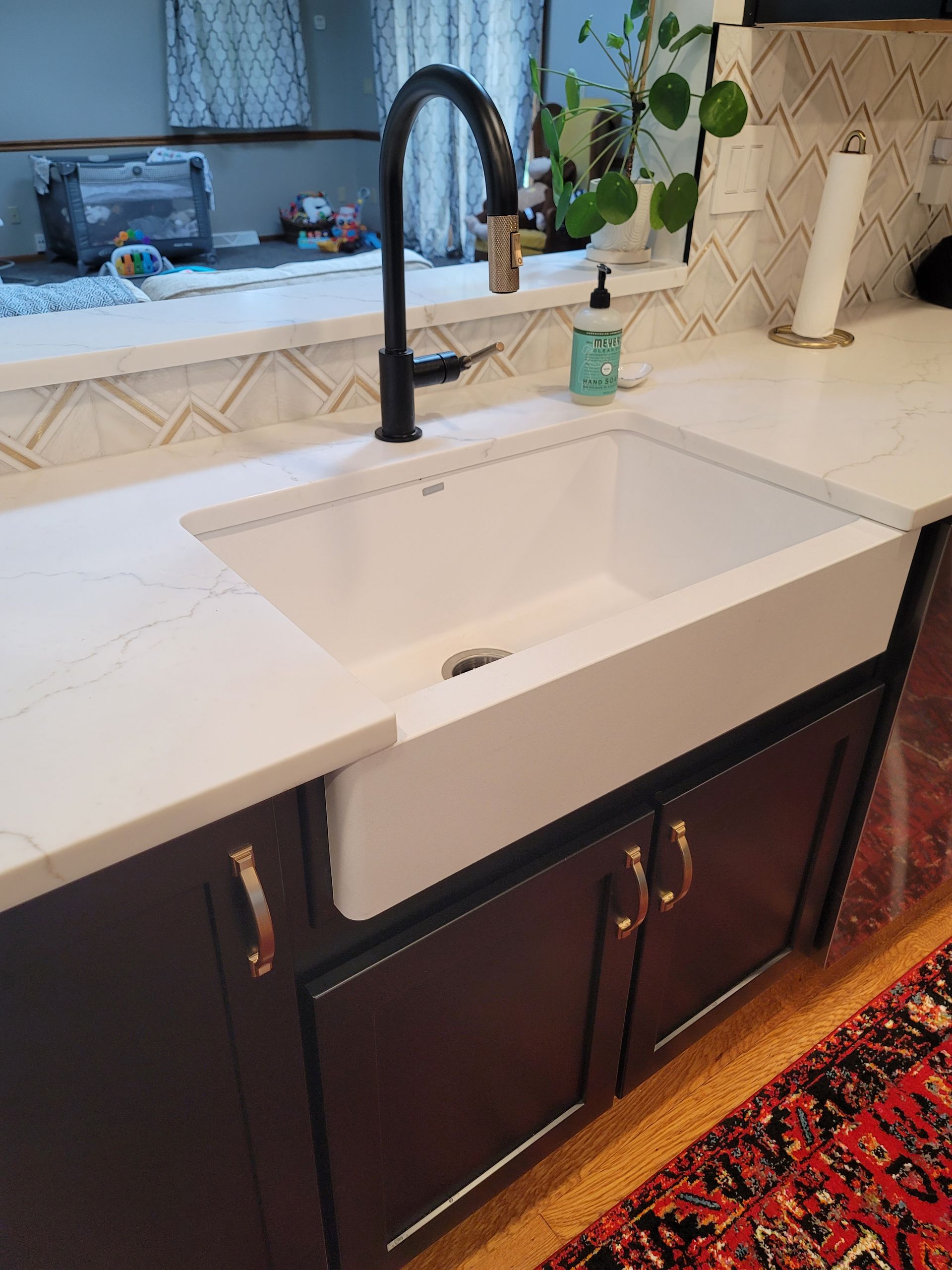 White farmhouse kitchen sink with black faucet, soap dispenser, and dark cabinets.